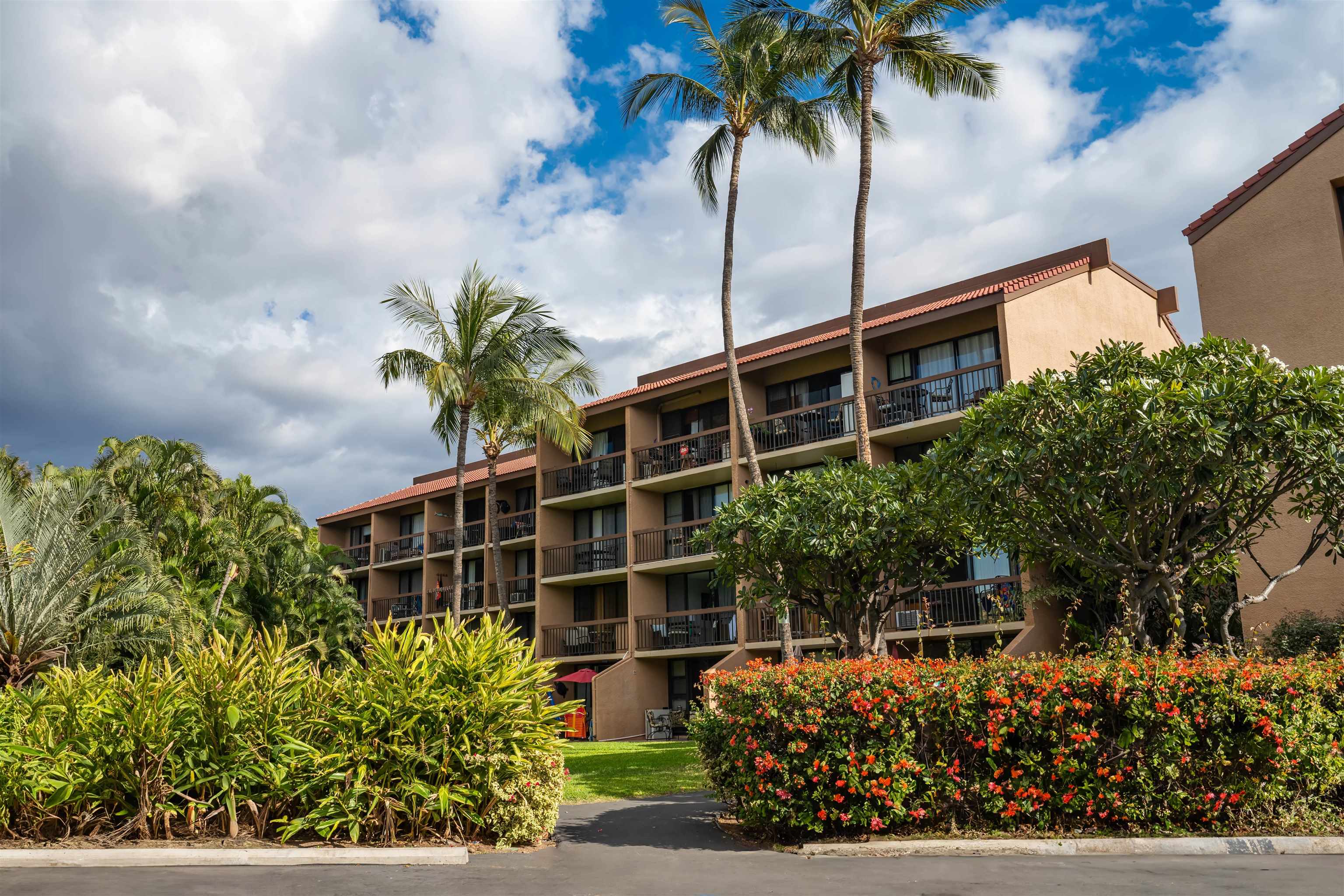 Condominium exterior with stacked balconies, tall palms, and colorful flowering shrubs.