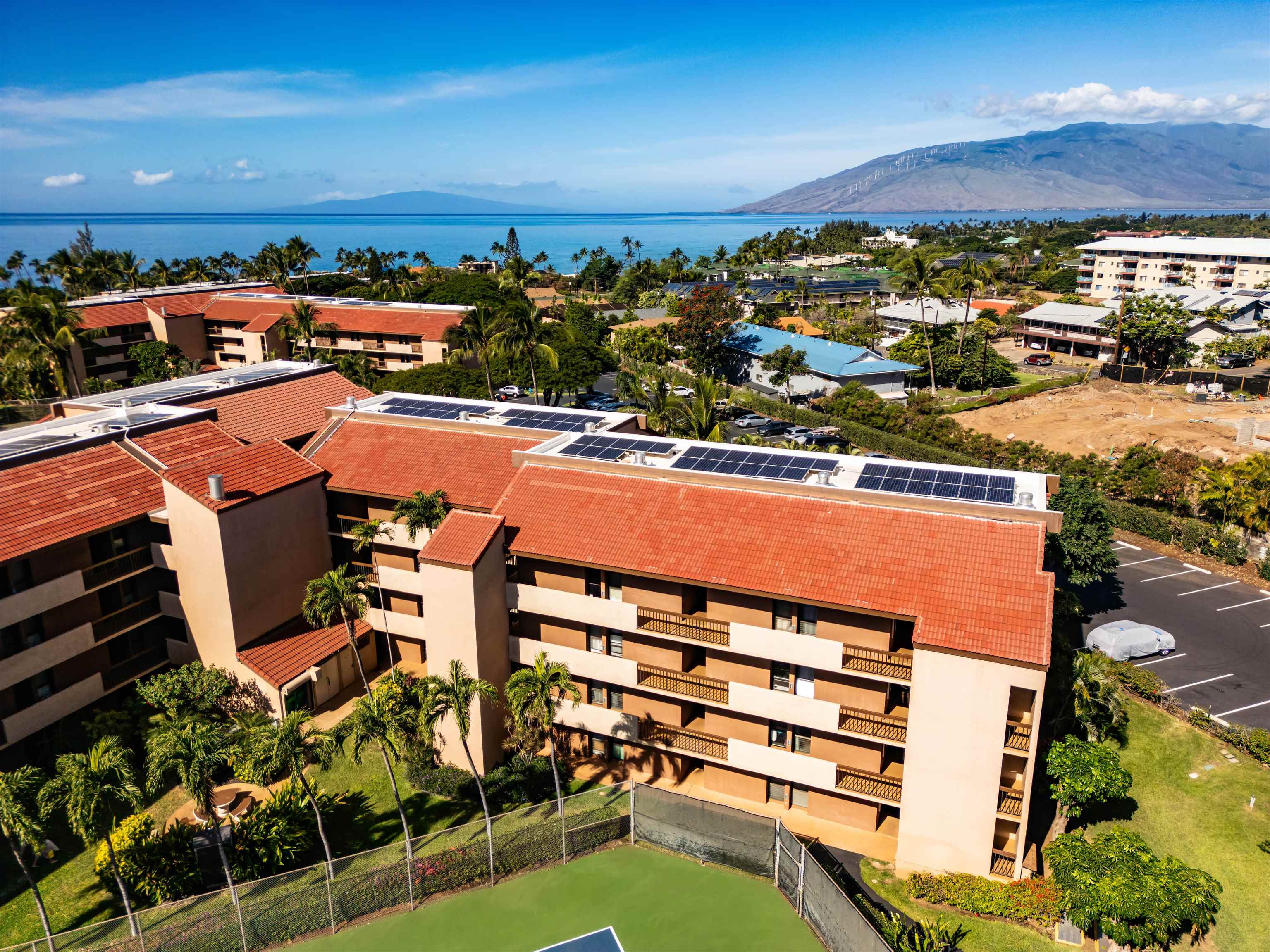 Condominium complex with solar panels and a tennis court, overlooking the ocean and distant mountains.