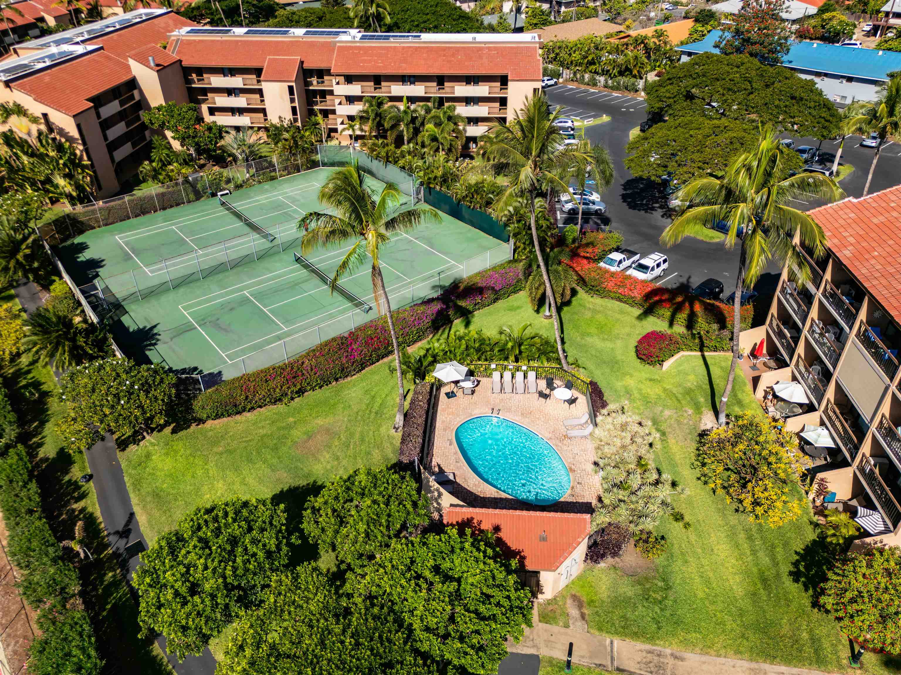 Aerial view of a condominium complex with a pool, tennis courts, and palm-lined grounds.