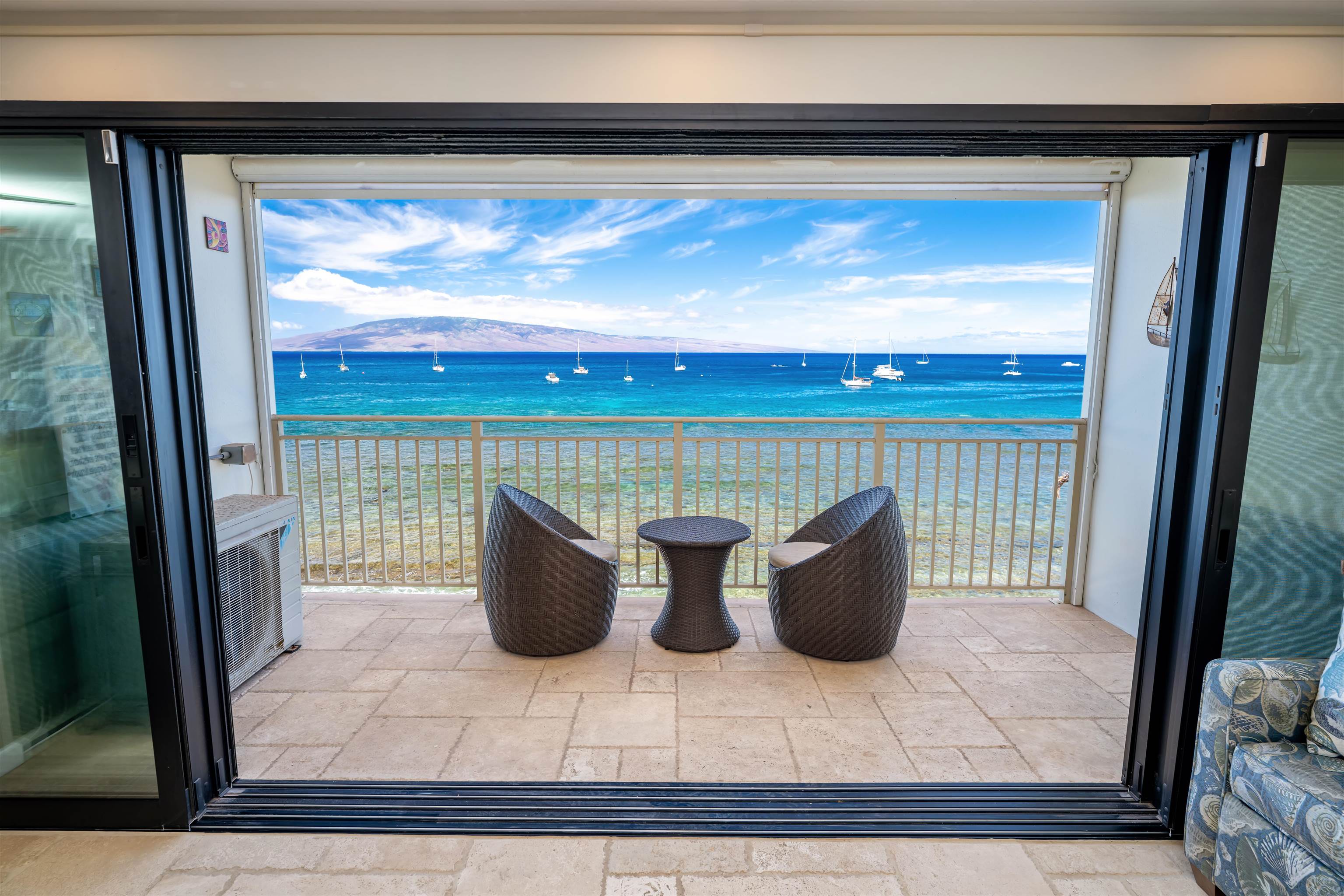 Apartment balcony with wicker seating overlooking sailboats, turquoise water, and a distant island ridge.