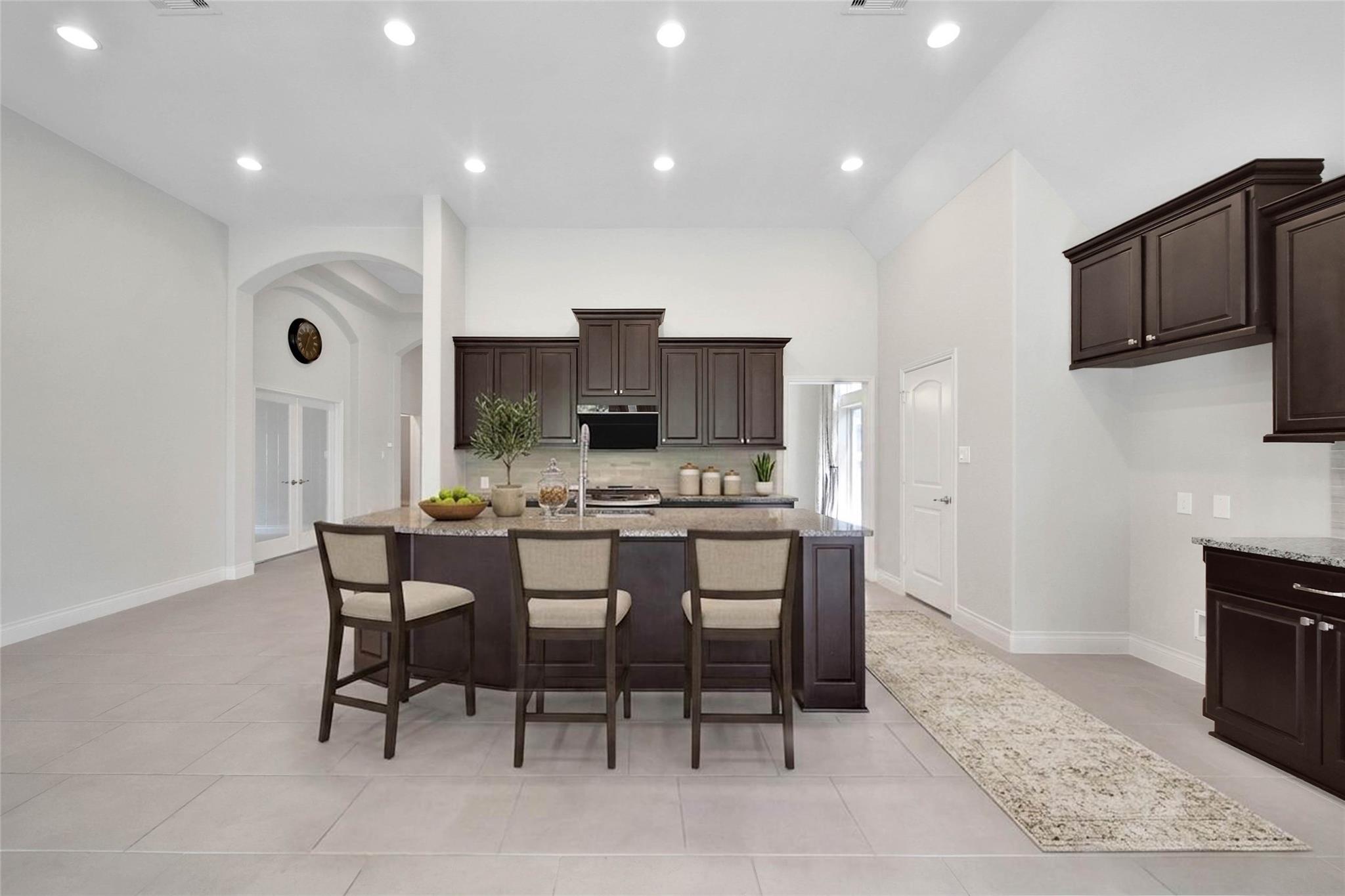 Kitchen with dark cabinetry and a large granite island with three bar stools.