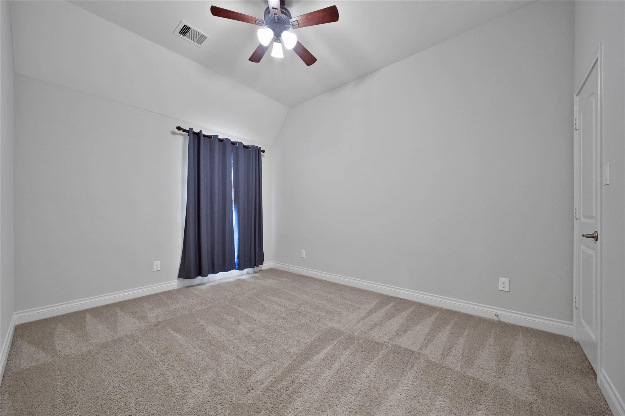 Empty carpeted bedroom with dark blue curtains and a ceiling fan with lights.