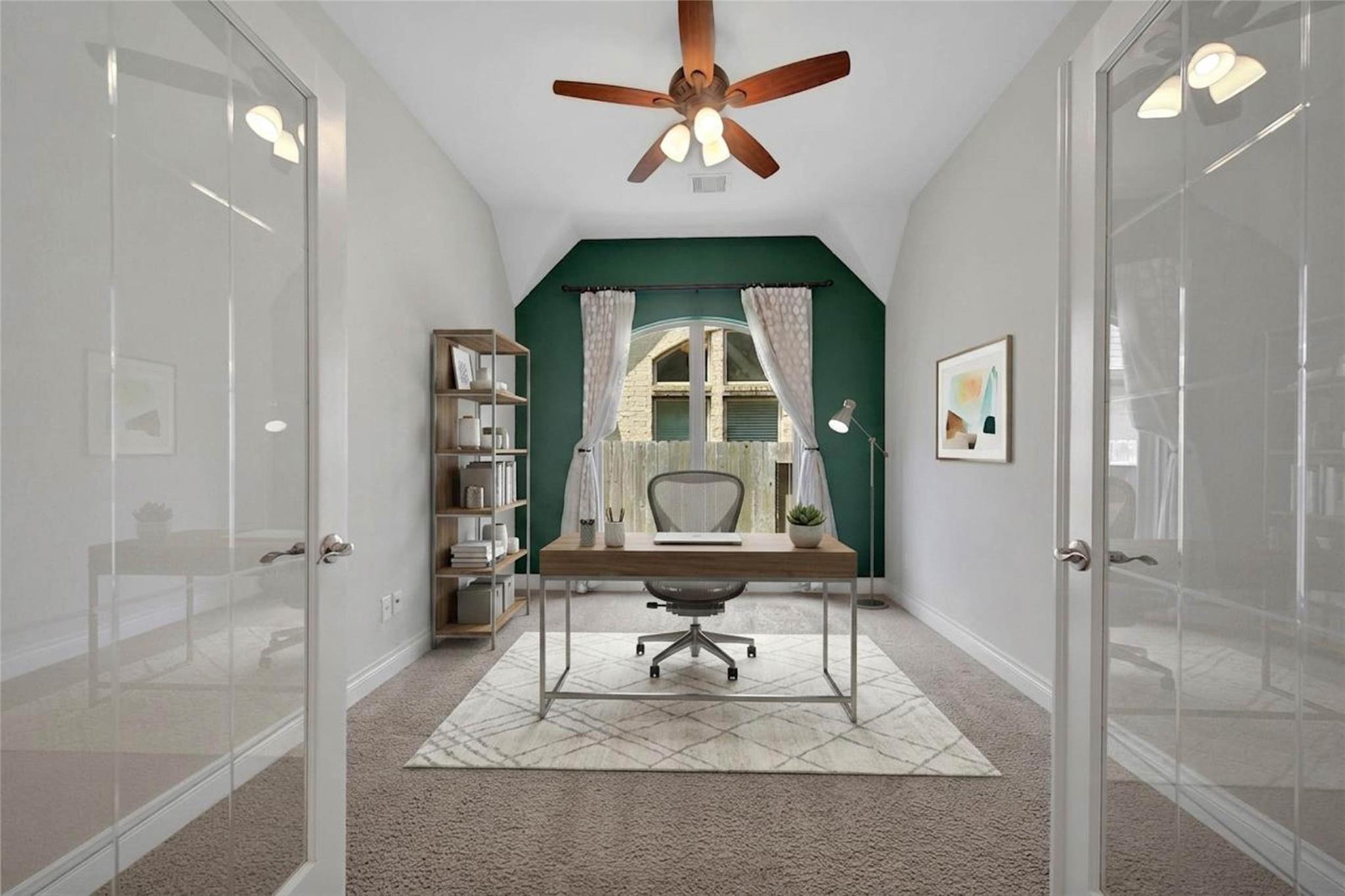 Furnished home office with a desk and chair against a green accent wall and curtained window.