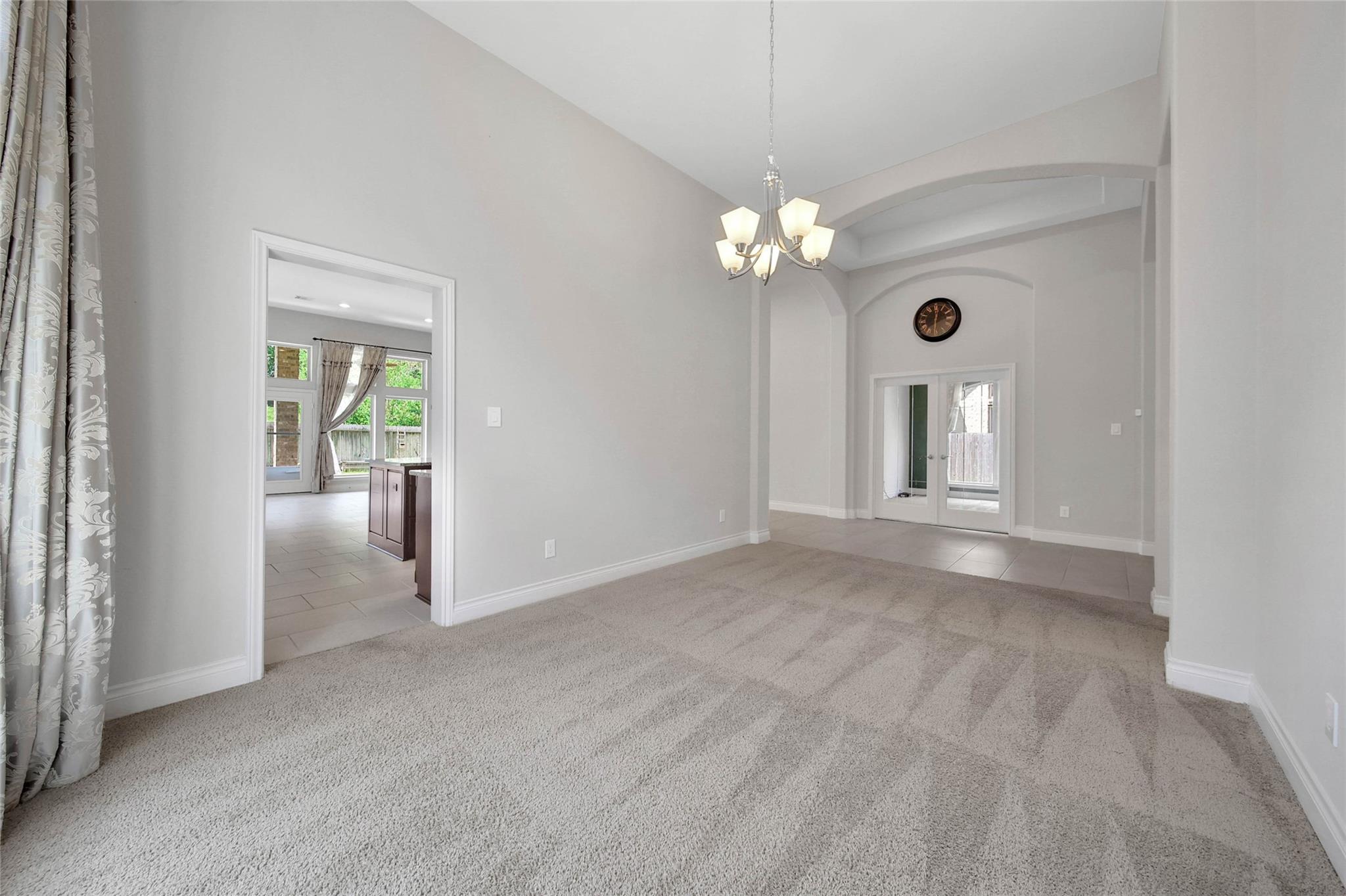 Empty carpeted dining room with a vaulted ceiling, chandelier, and arched details.