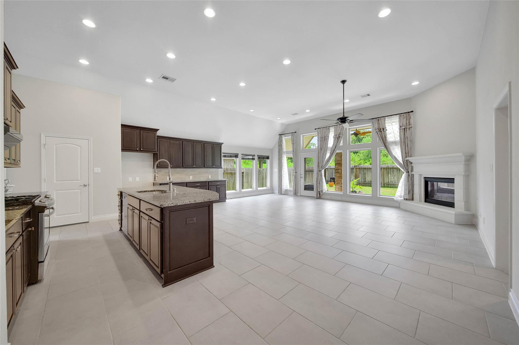 Open-plan kitchen and living area with dark cabinetry, granite island, tall windows, and fireplace.