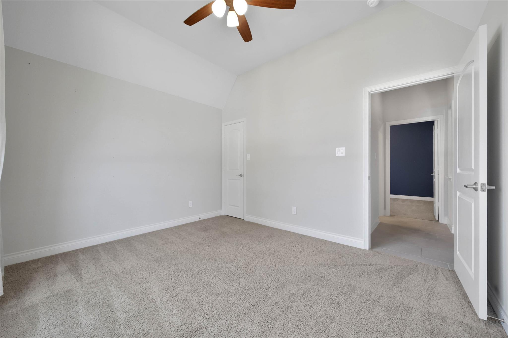 Empty carpeted bedroom with a vaulted ceiling, ceiling fan, and open doorway to the hall.