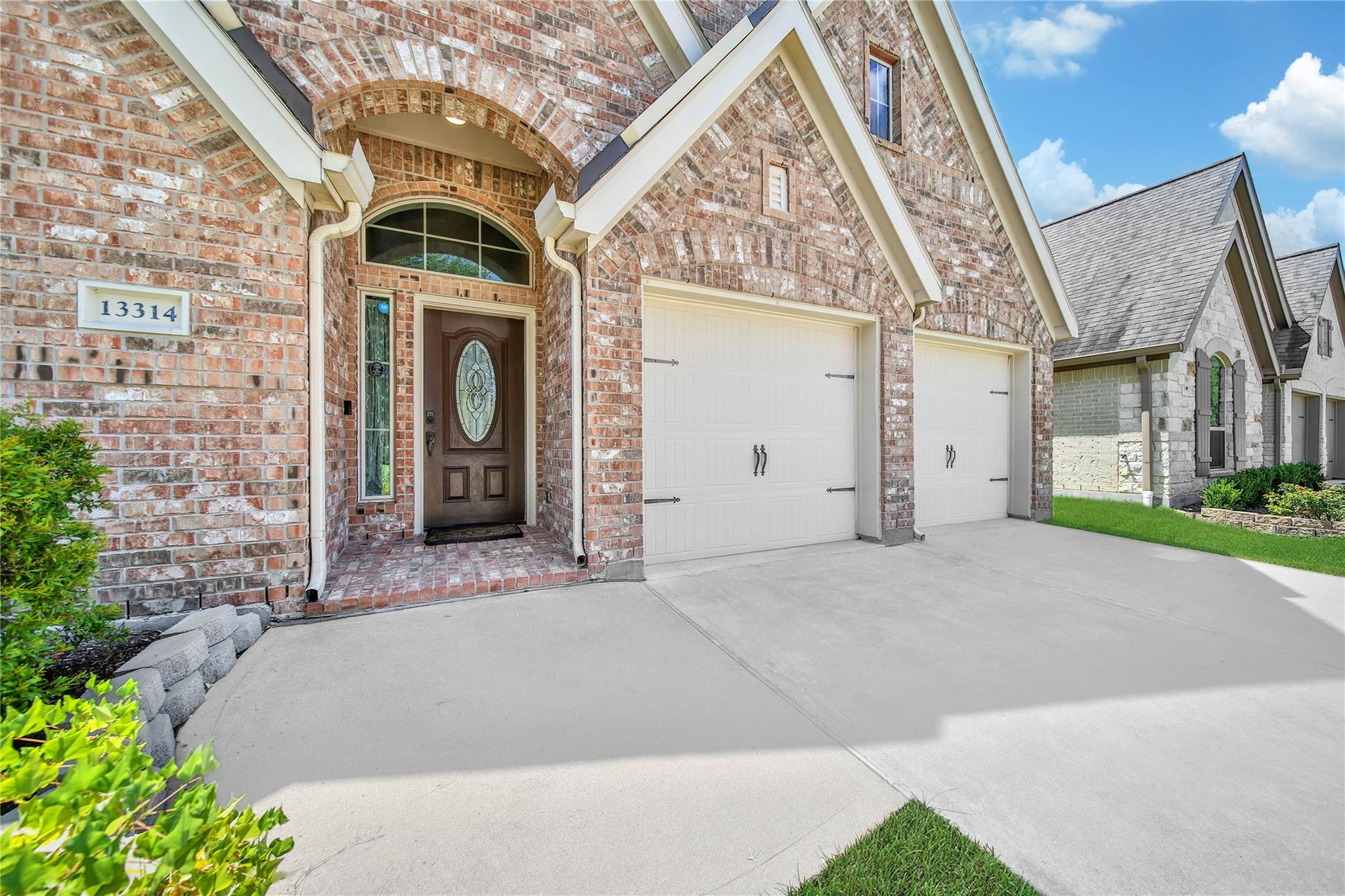 Red brick home with an arched entry, decorative glass front door, and two white garage doors.