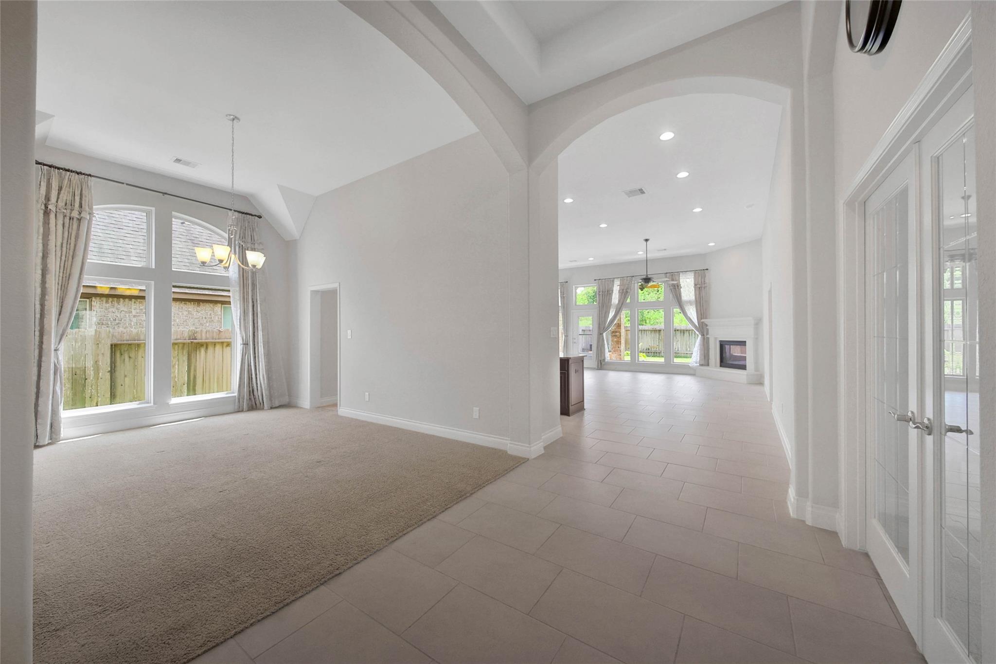 Open sitting area and tiled hallway lead to a living room with large windows and a fireplace.