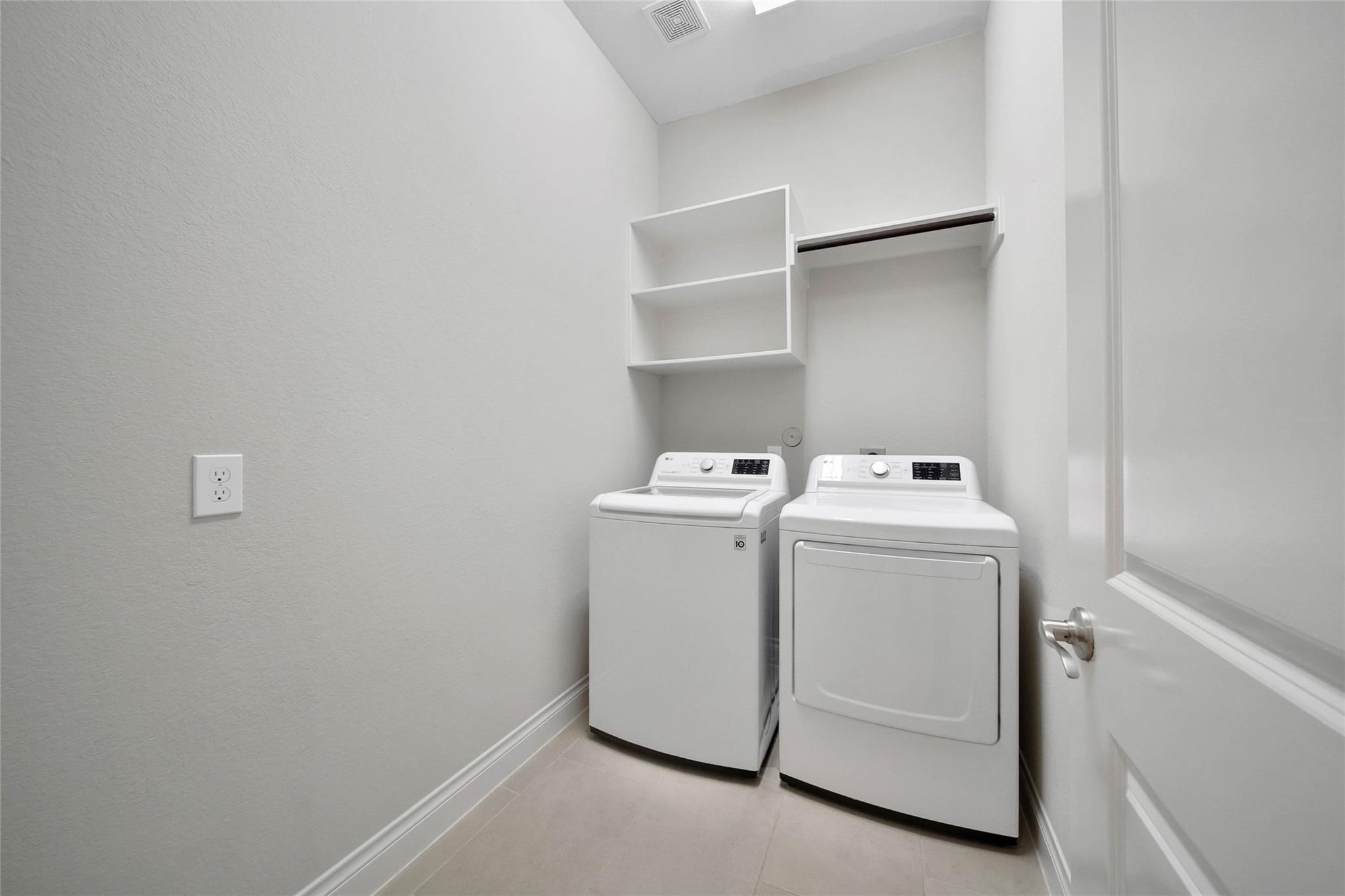 Laundry room with side-by-side white washer and dryer beneath open shelving and a hanging rod.