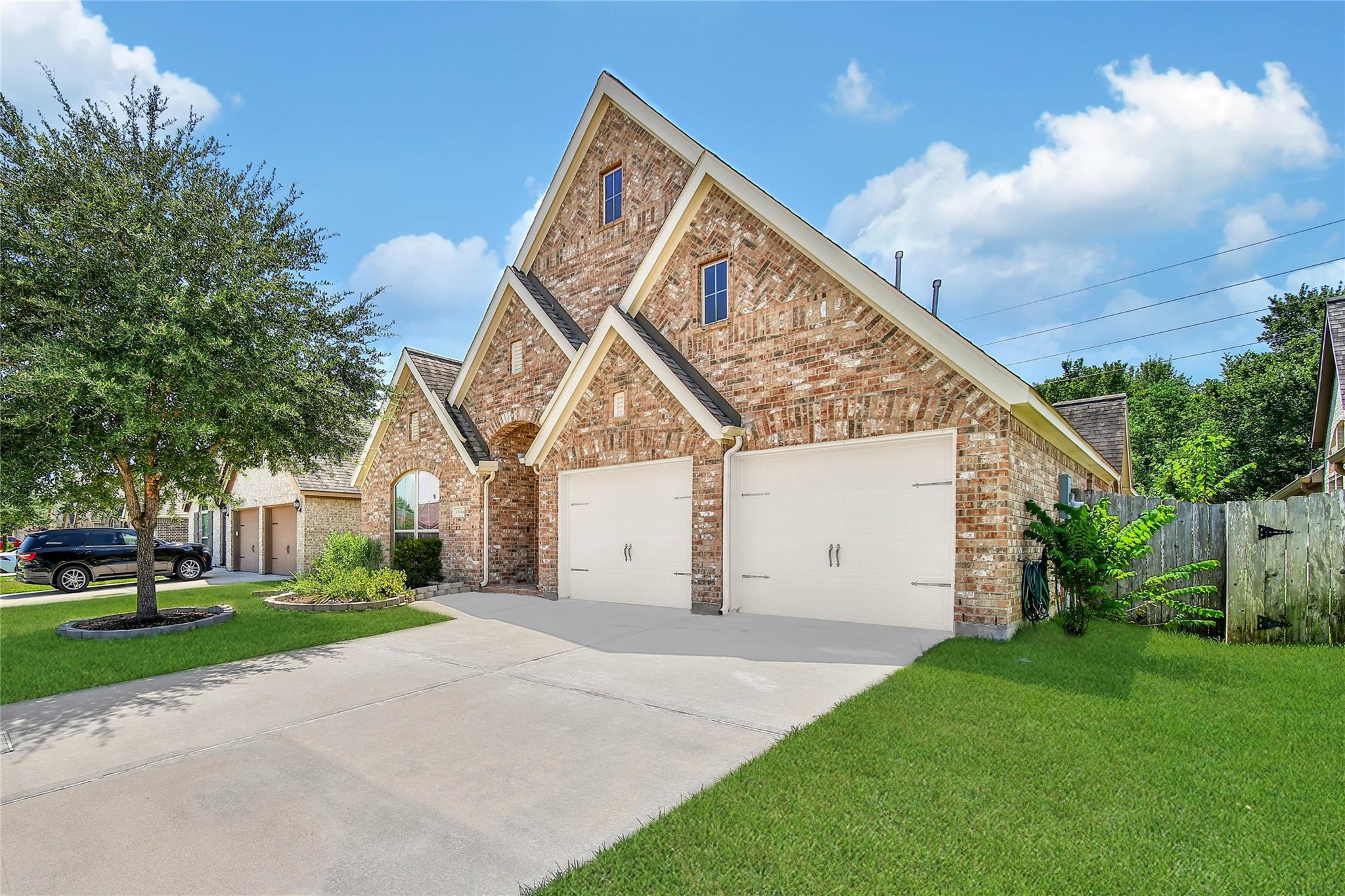 Two-story brick house with steep gables, two garage doors, and a wide driveway.