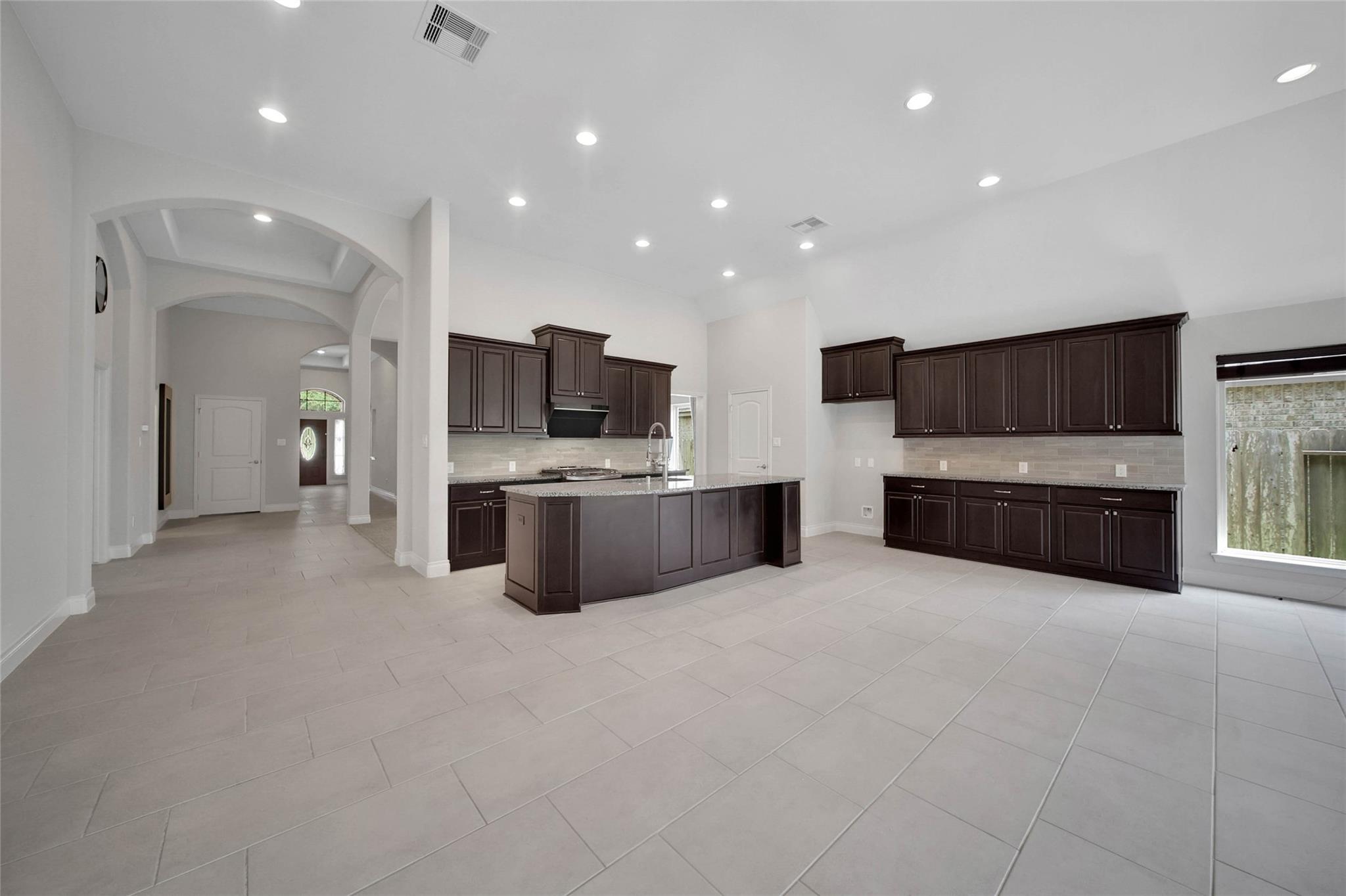 Kitchen with dark brown cabinets, a large island, light tile floors, and arched openings to the entry hall.