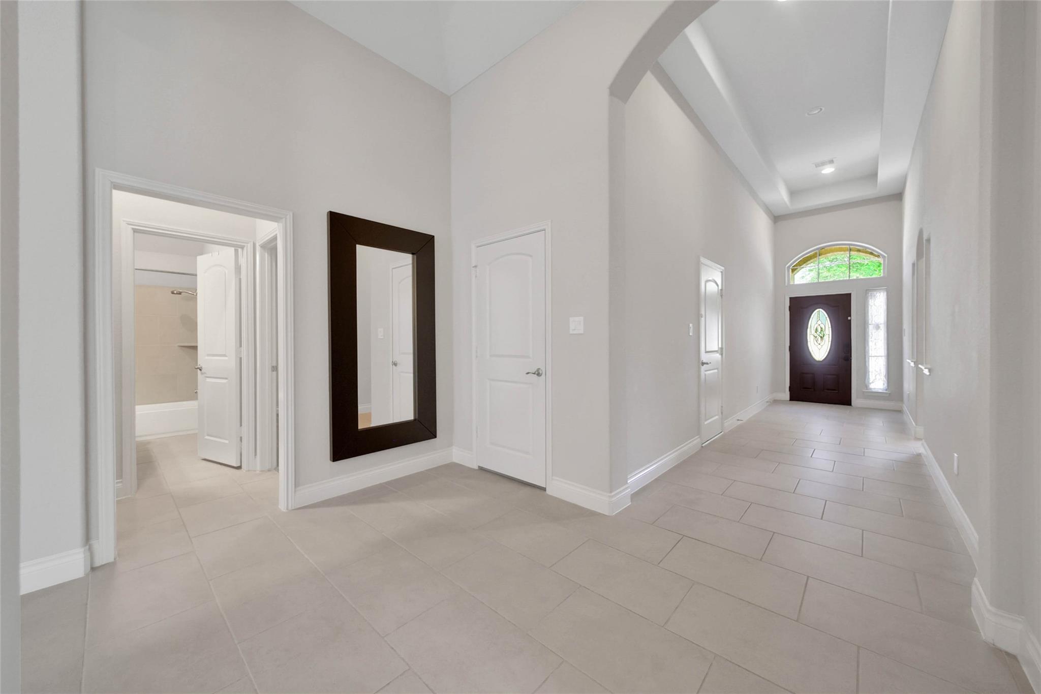 Foyer with large tile floors, a dark glass-paneled front door, and an arched transom window.