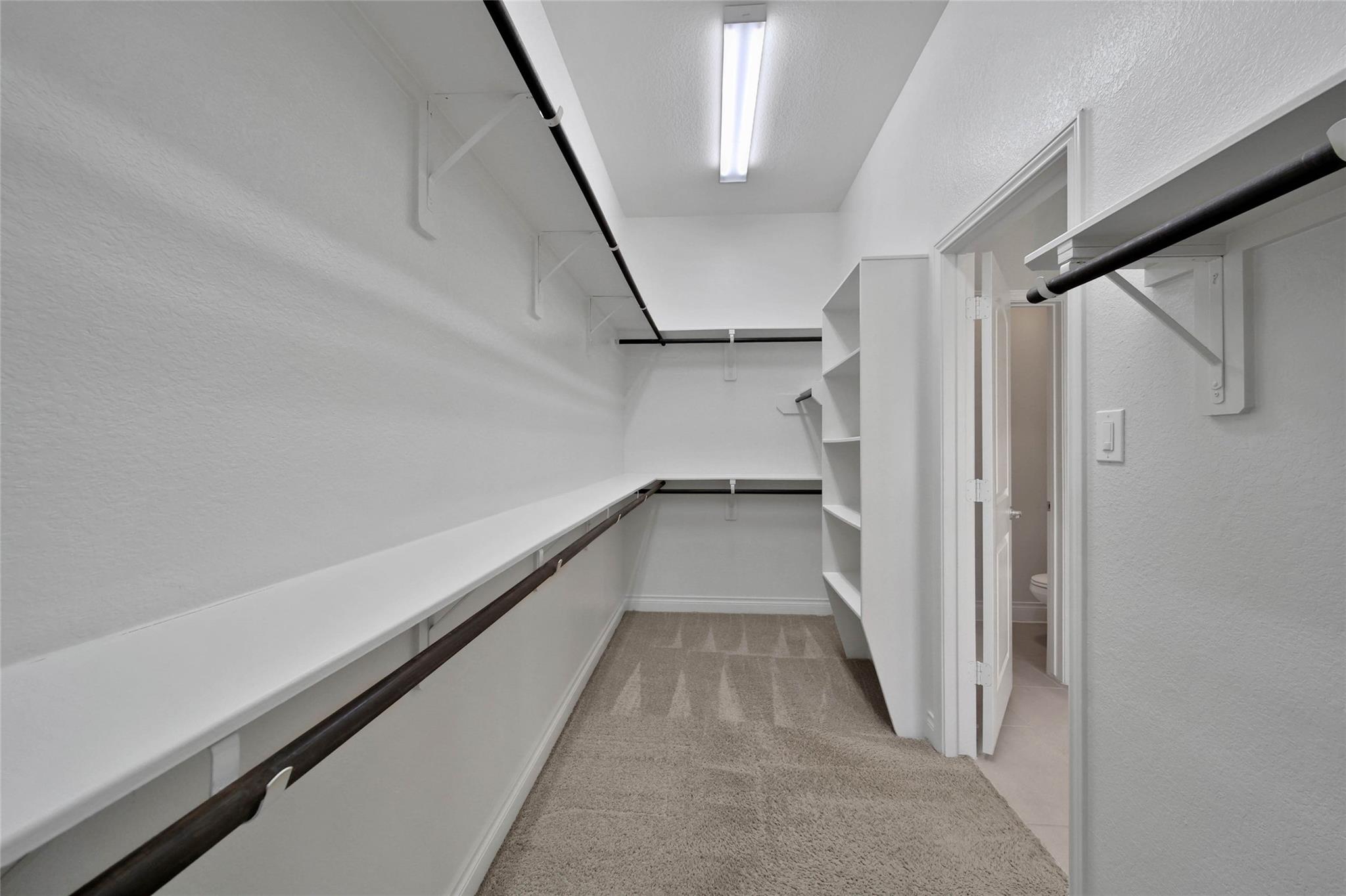 Walk-in closet with wraparound shelves, dark hanging rods, and a bathroom doorway.