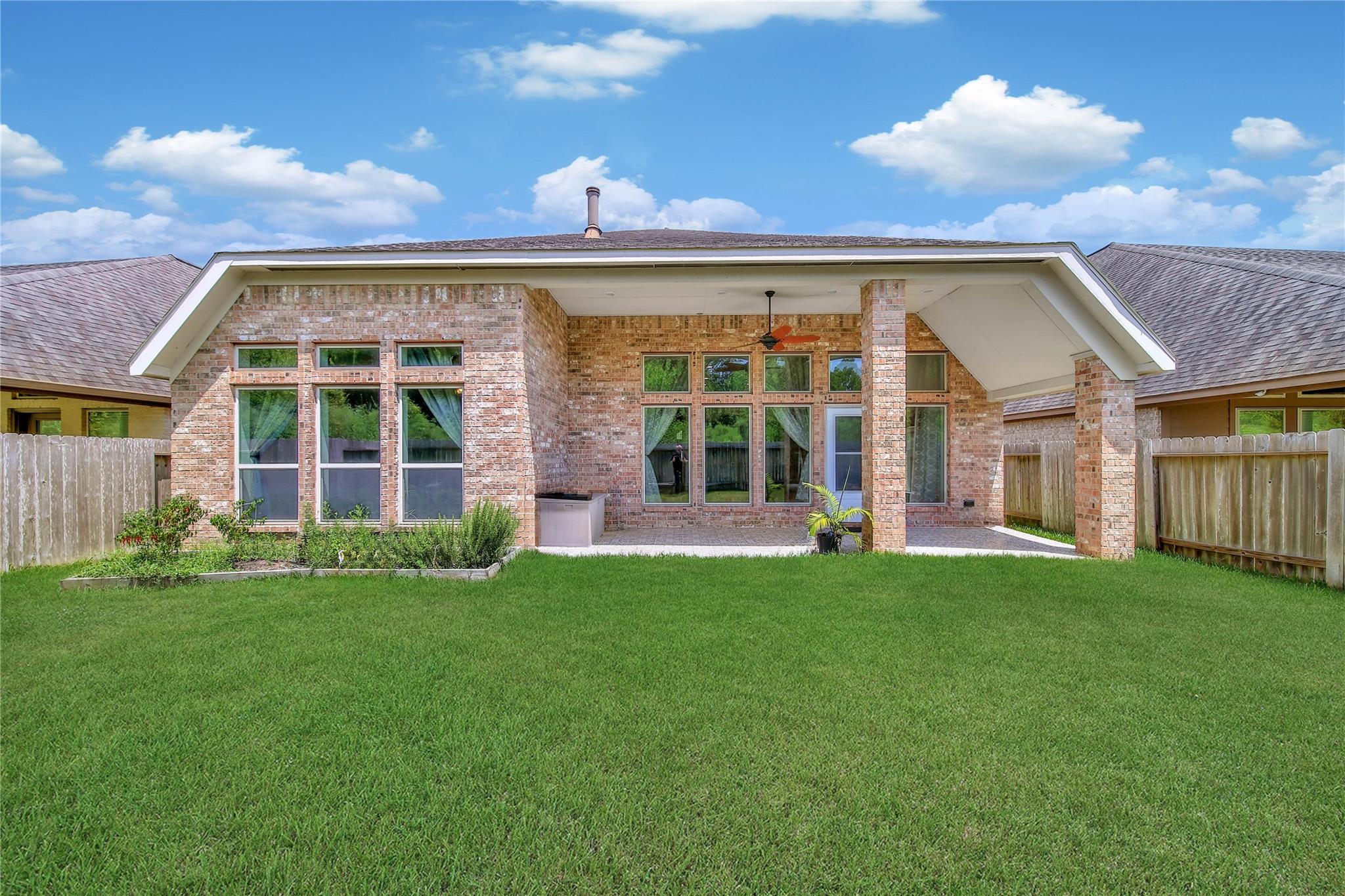 Brick house rear exterior with a covered patio and wide fenced lawn.