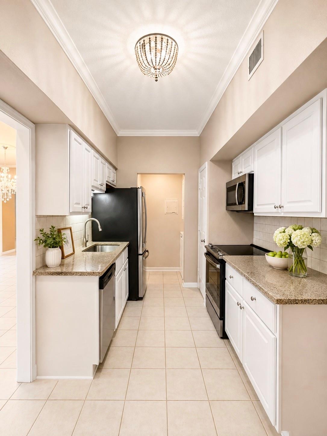 Galley kitchen with white cabinets, granite counters, black appliances, and a crystal chandelier.