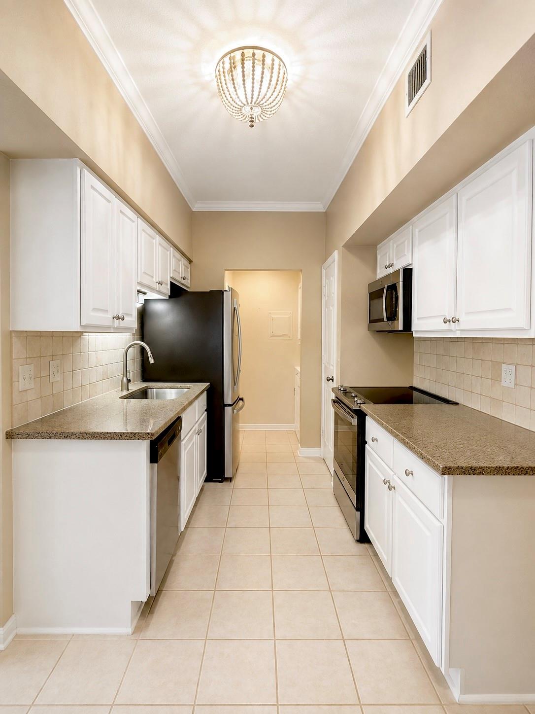 Galley kitchen with white cabinets, granite counters, black appliances, and a high ceiling with a chandelier.
