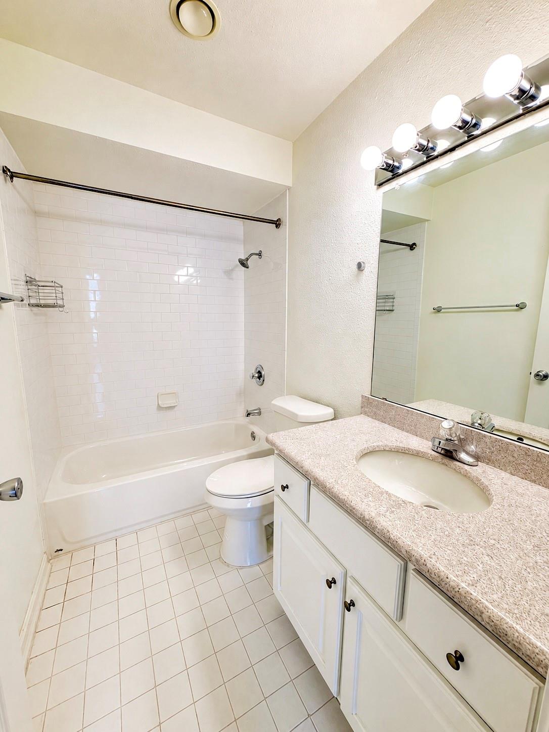 Bathroom with a white tub and tiled shower beside a white vanity and large mirror.