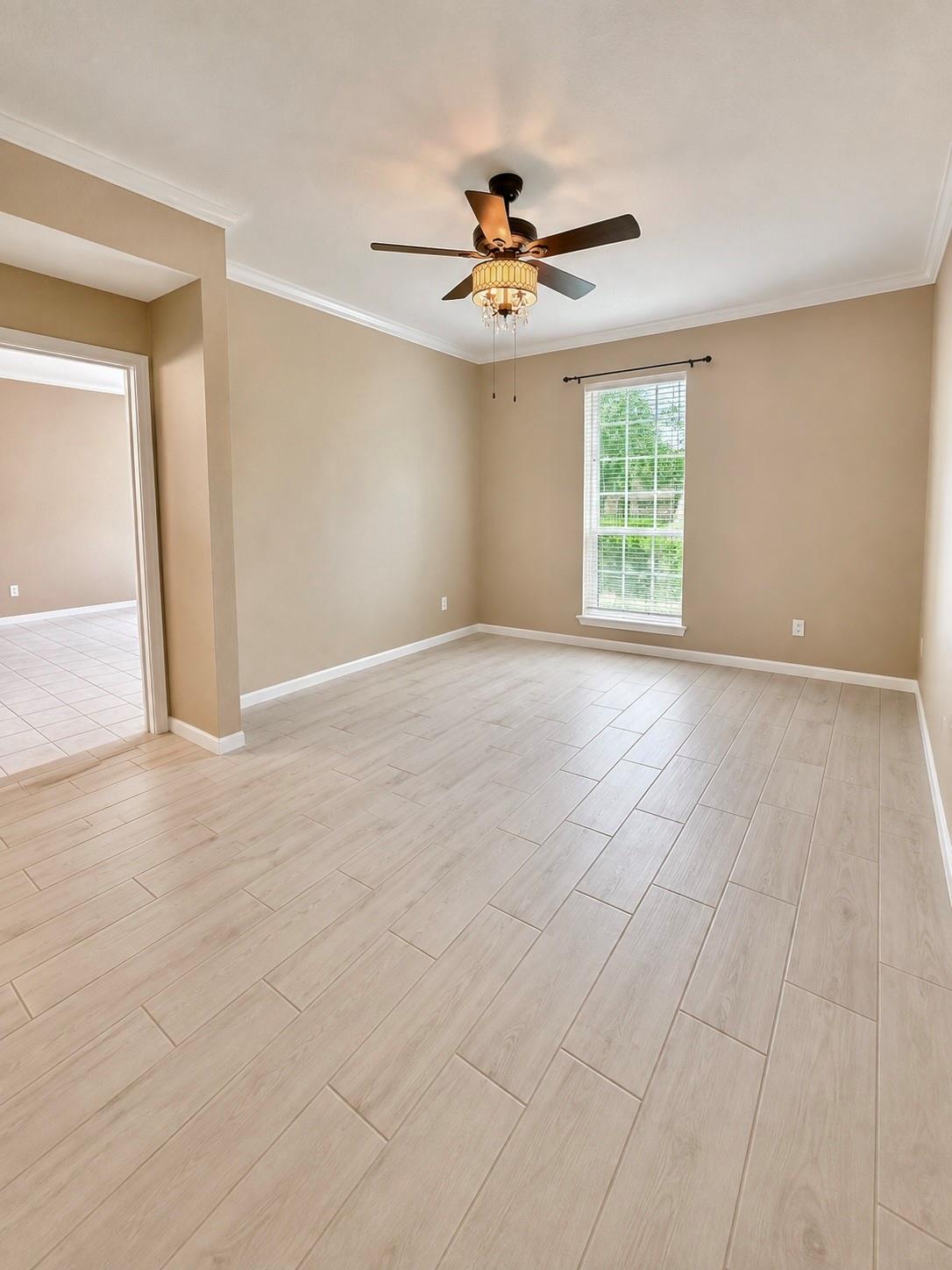 Empty room with pale wood-look tile flooring, a ceiling fan, and a window overlooking greenery.