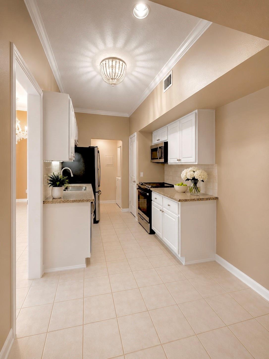 Galley kitchen with white cabinets, beige tile floors, and black appliances.