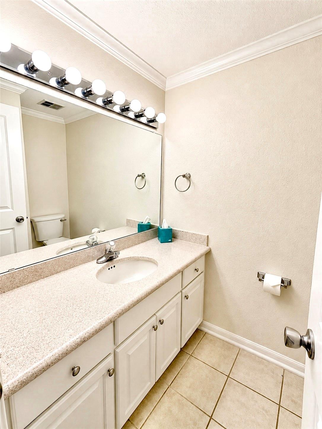Bathroom vanity with a long countertop, white cabinets, large mirror, and tiled floor.