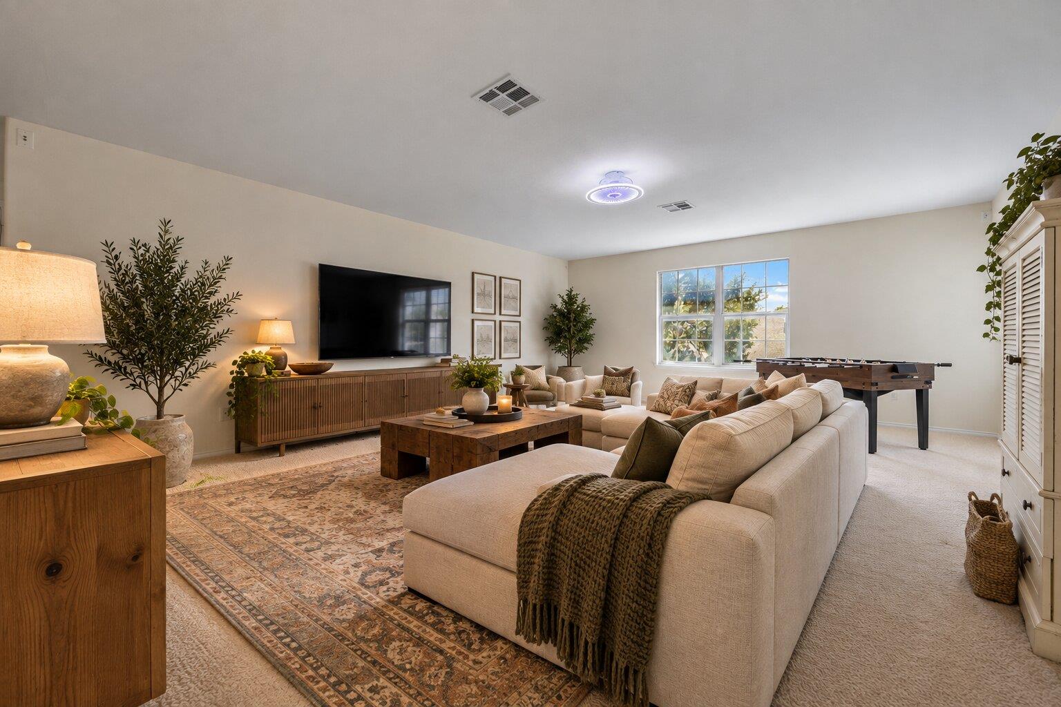 Living room with a cream sectional, patterned rug, and foosball table beside a bright window.