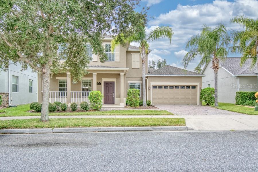 Two-story beige house with a covered porch, attached garage, and palm trees.