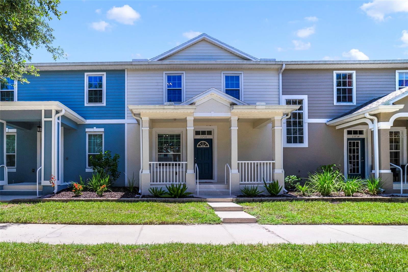 Two-story townhouse with blue and gray siding, a covered porch, and a landscaped entry.