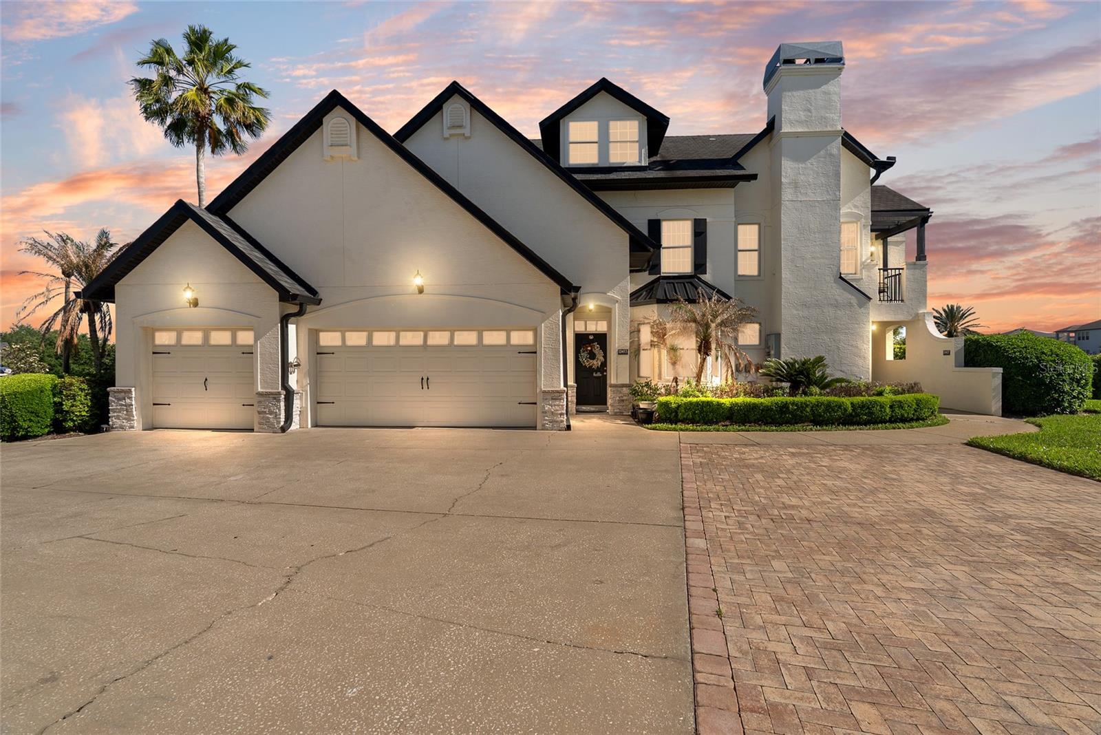 Large white multi-story house with a tall chimney and two garage doors at dusk.