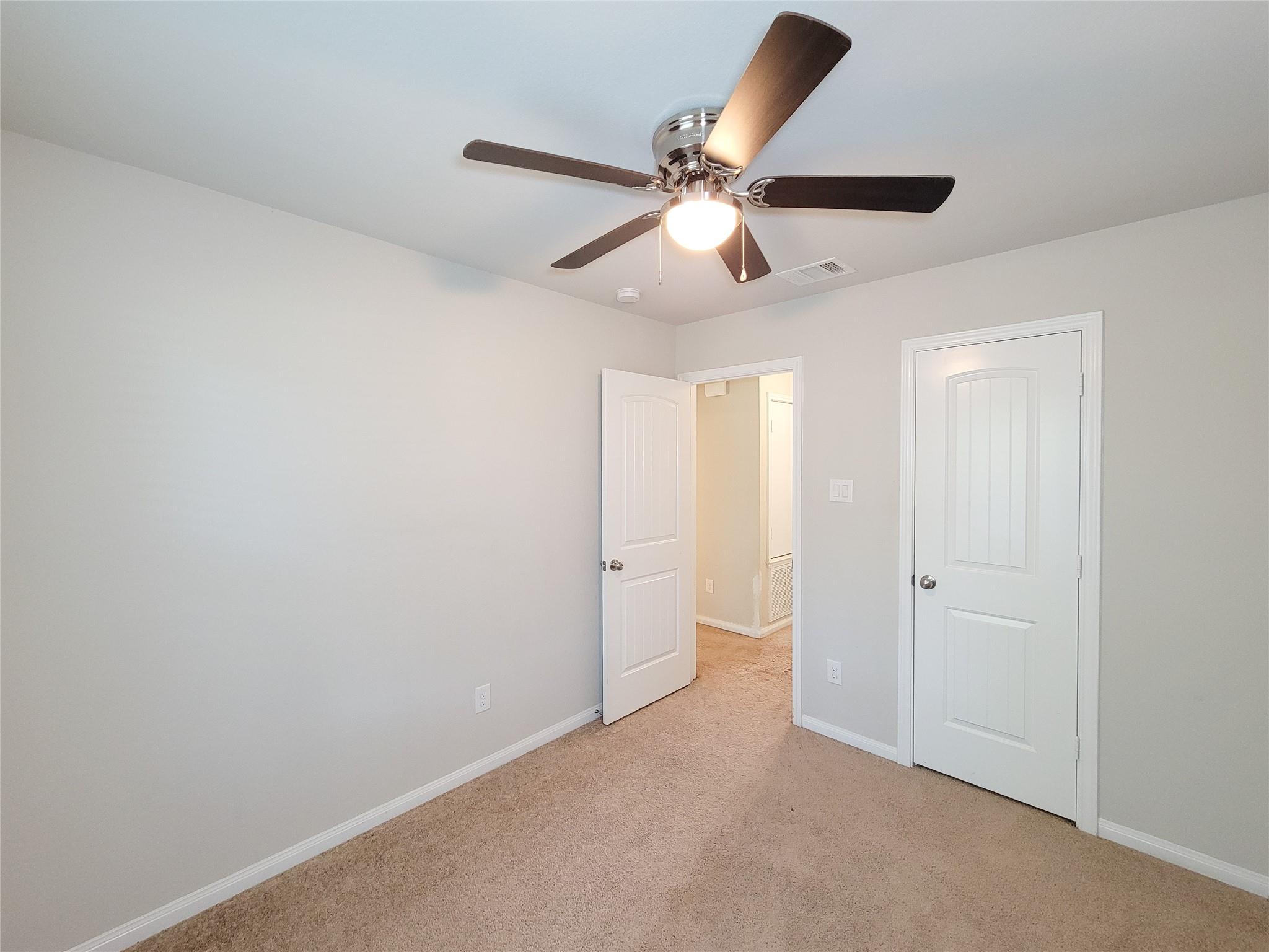 Empty carpeted bedroom with a ceiling fan and an open doorway to the hall.