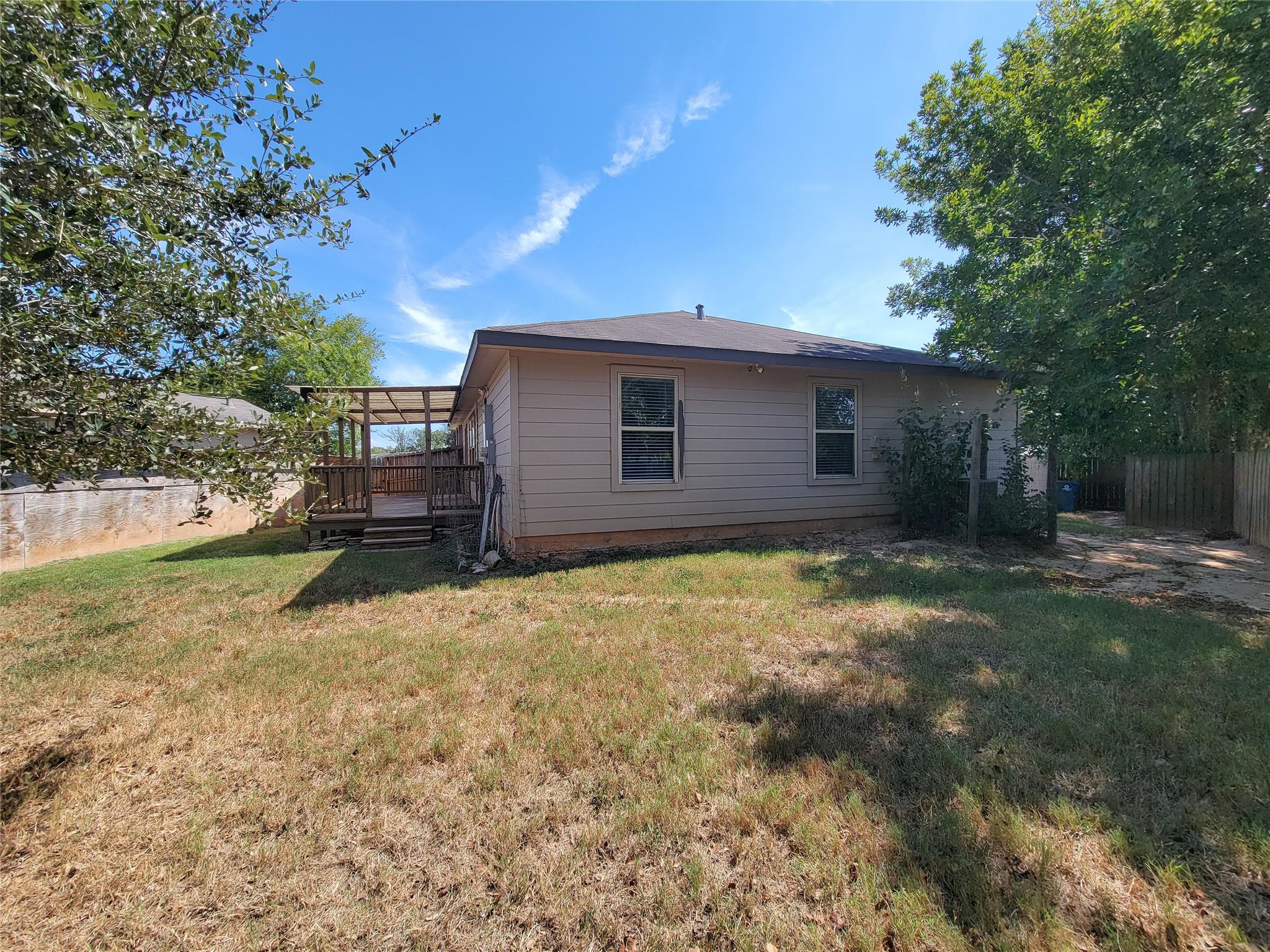 House rear exterior with a covered wooden deck, fenced yard, and mature shade trees.
