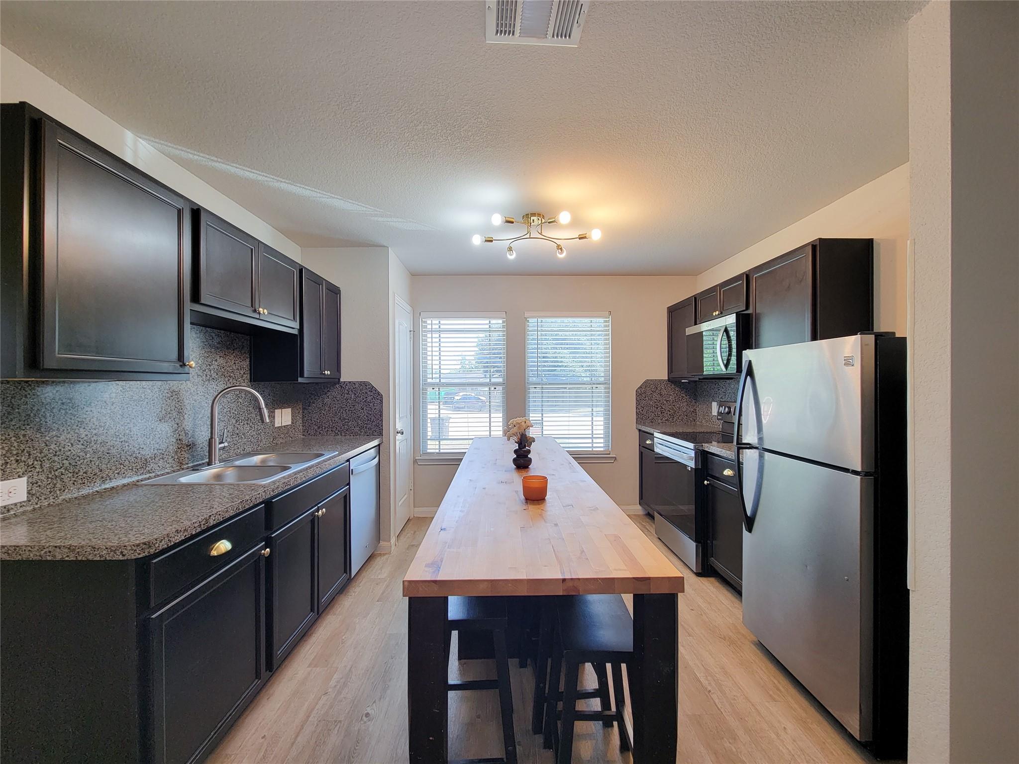 Kitchen with dark cabinets, stainless steel appliances, and a long butcher-block island with stools.