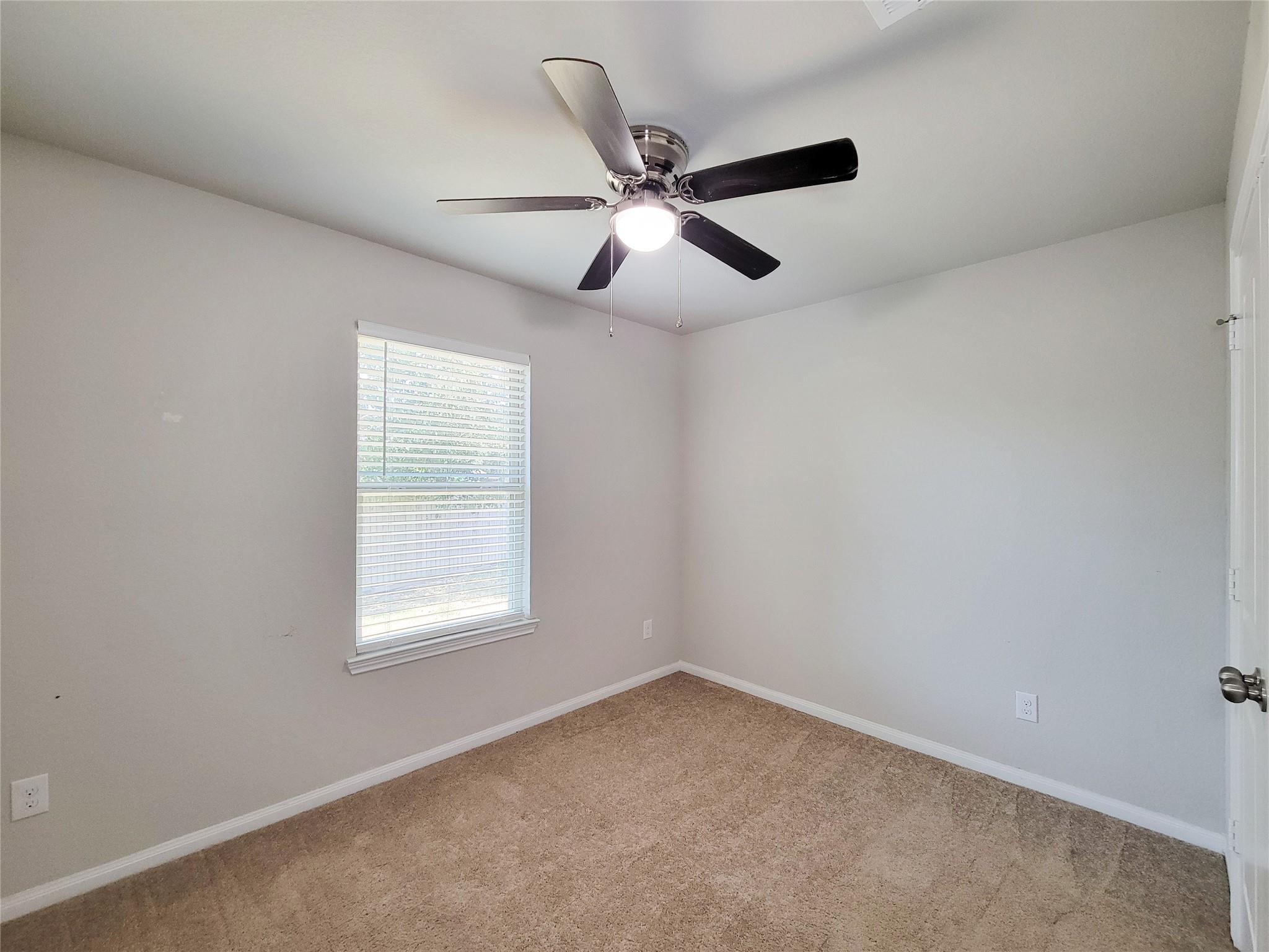 Empty carpeted room with a window and a ceiling fan with light.