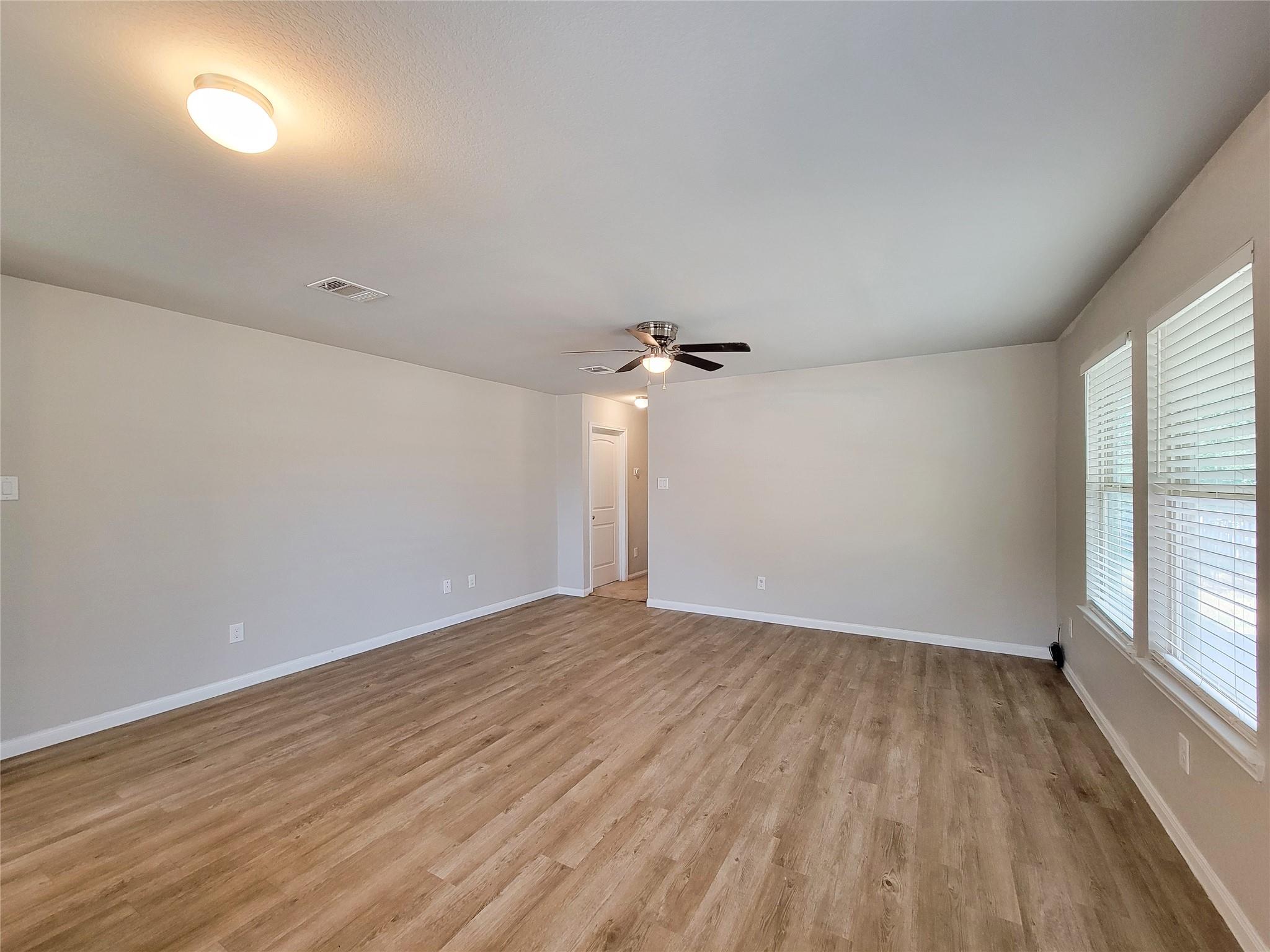 Vacant room with wood-look flooring, two blind-covered windows, and a ceiling fan.