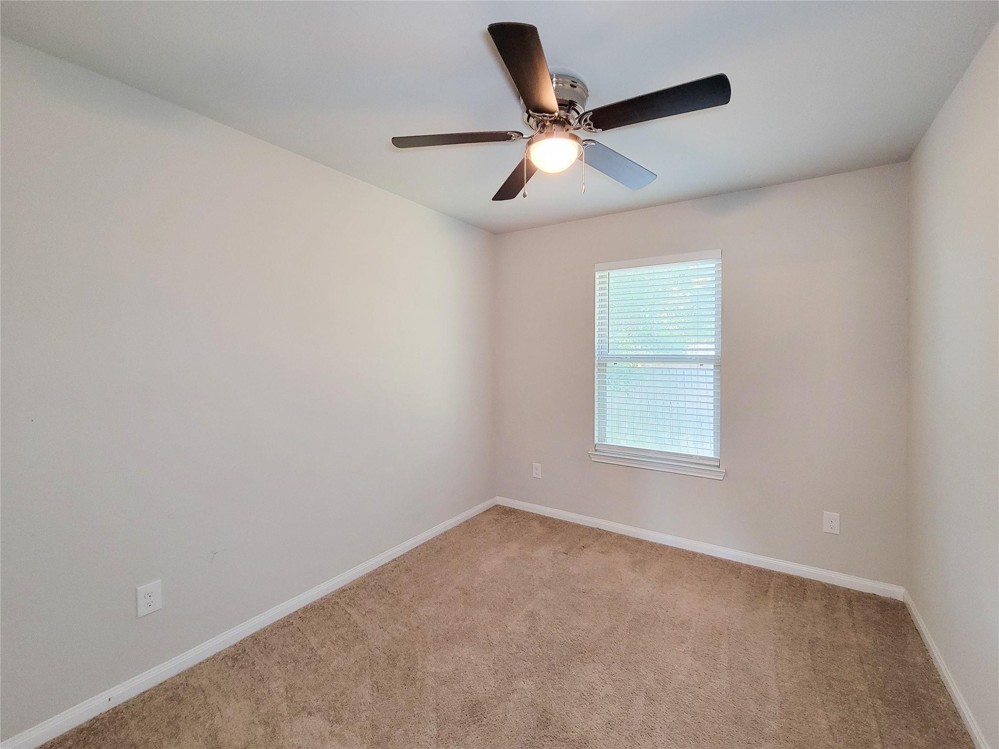 Empty bedroom with beige carpet, a window with white blinds, and a ceiling fan.