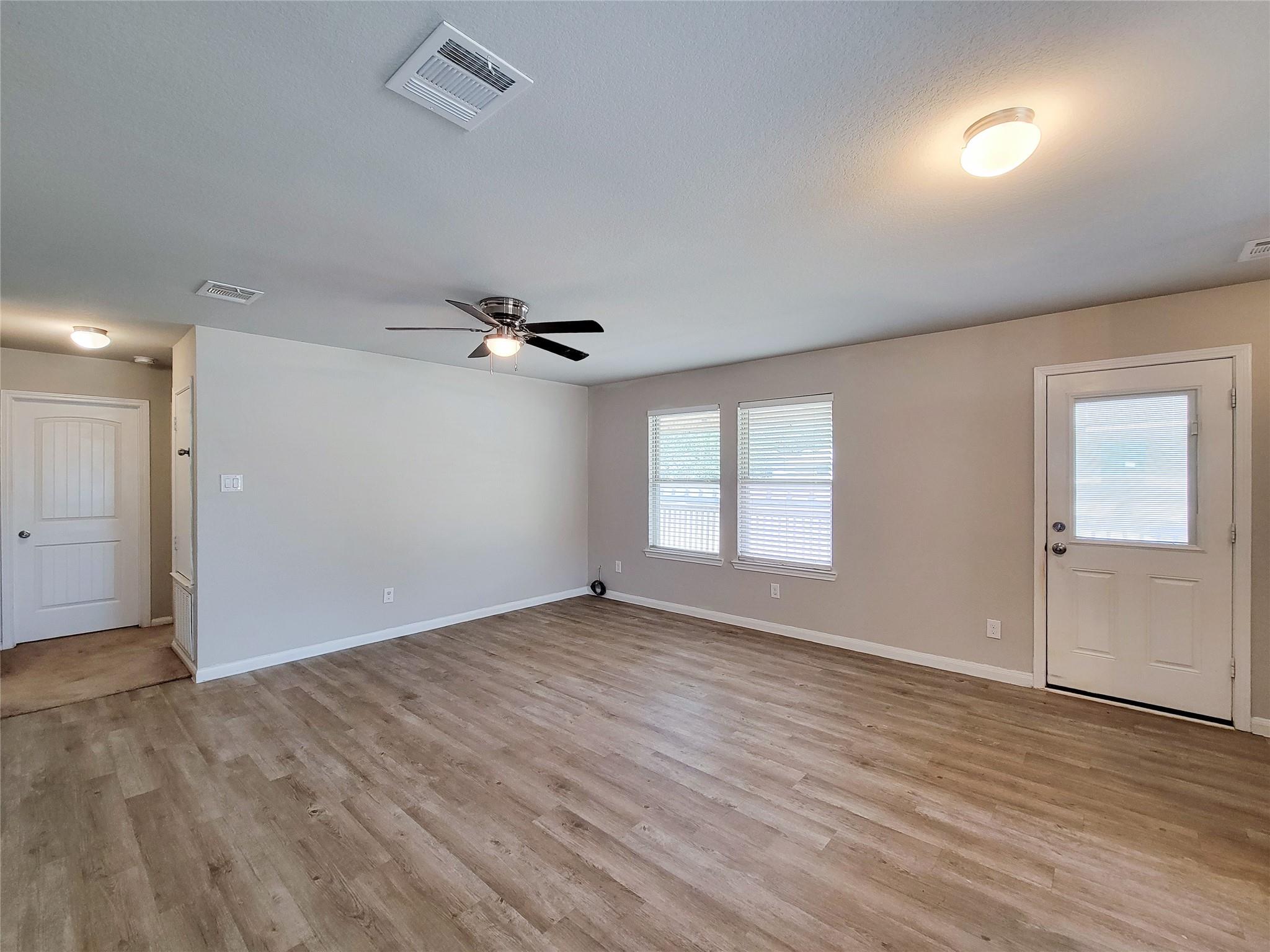 Vacant living room with wood-look flooring, a ceiling fan, and two windows with blinds.