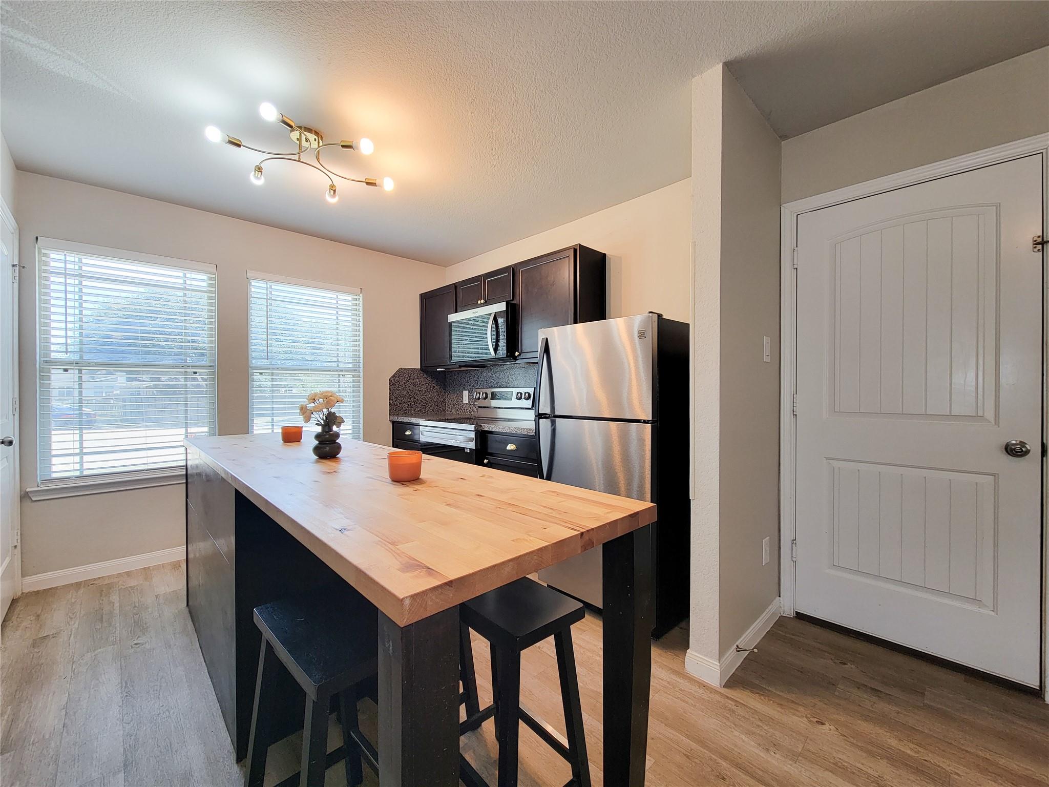 Kitchen with a butcher-block island, black stools, dark cabinets, and stainless steel appliances.