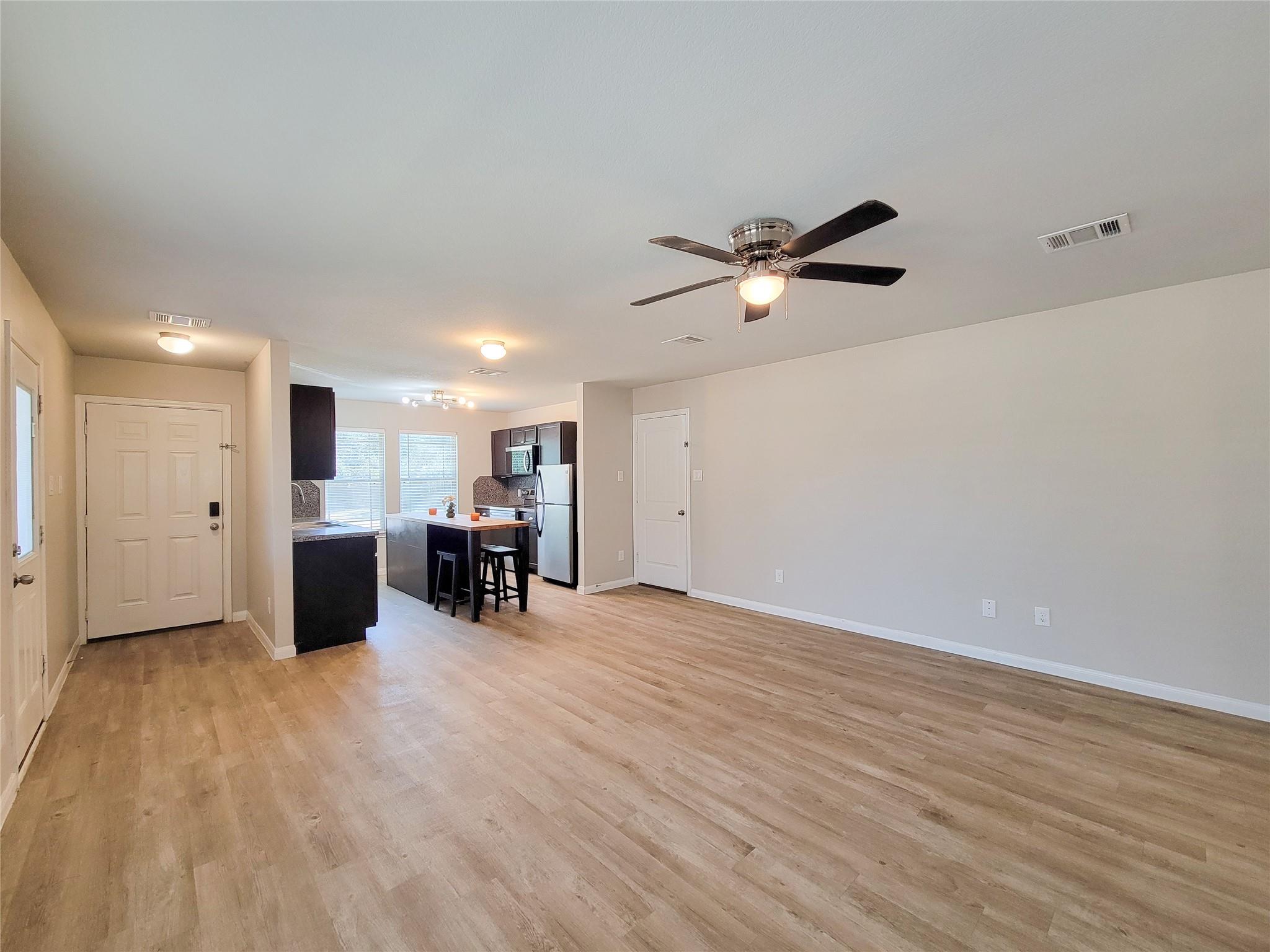 Open-plan living room and kitchen with wood-look floors, dark cabinets, and a breakfast bar.