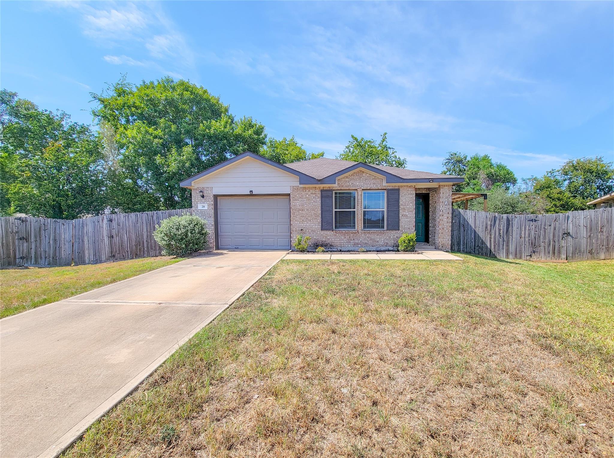 Single-story brick home with a long driveway, fenced yard, and green front door.