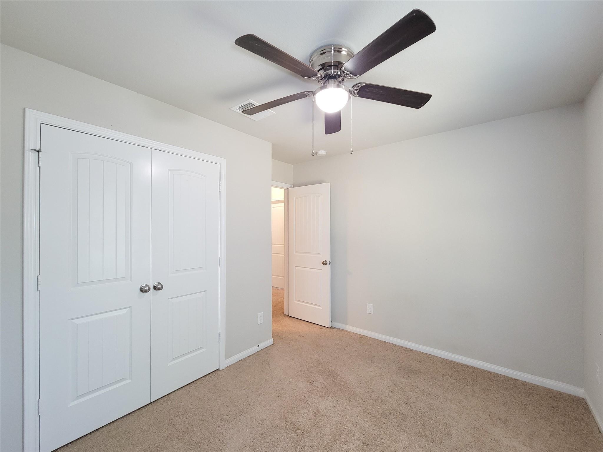 Empty carpeted bedroom with white closet doors and a ceiling fan with light.
