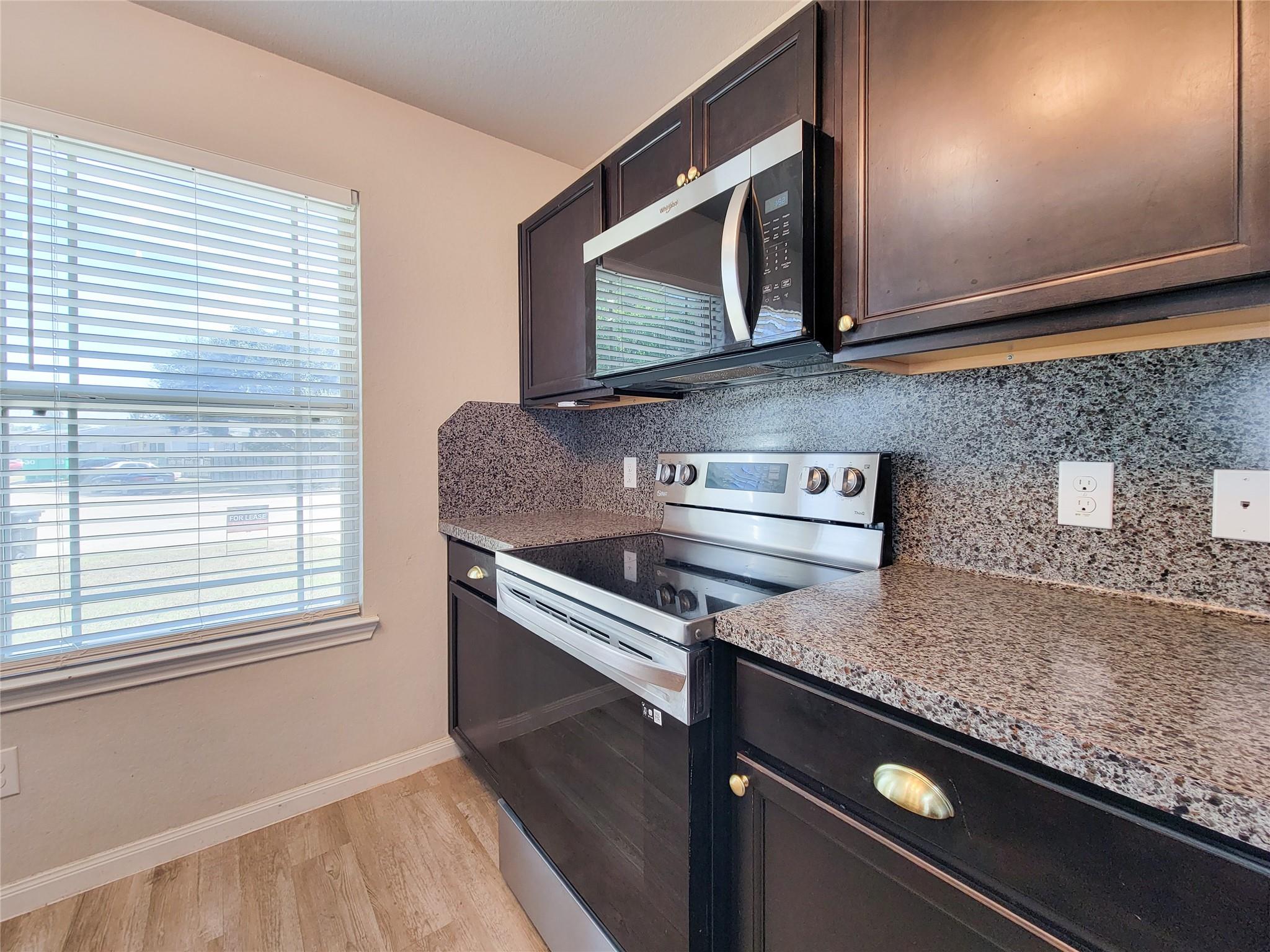 Kitchen with dark cabinets, speckled granite counters, and a stainless steel range and microwave.
