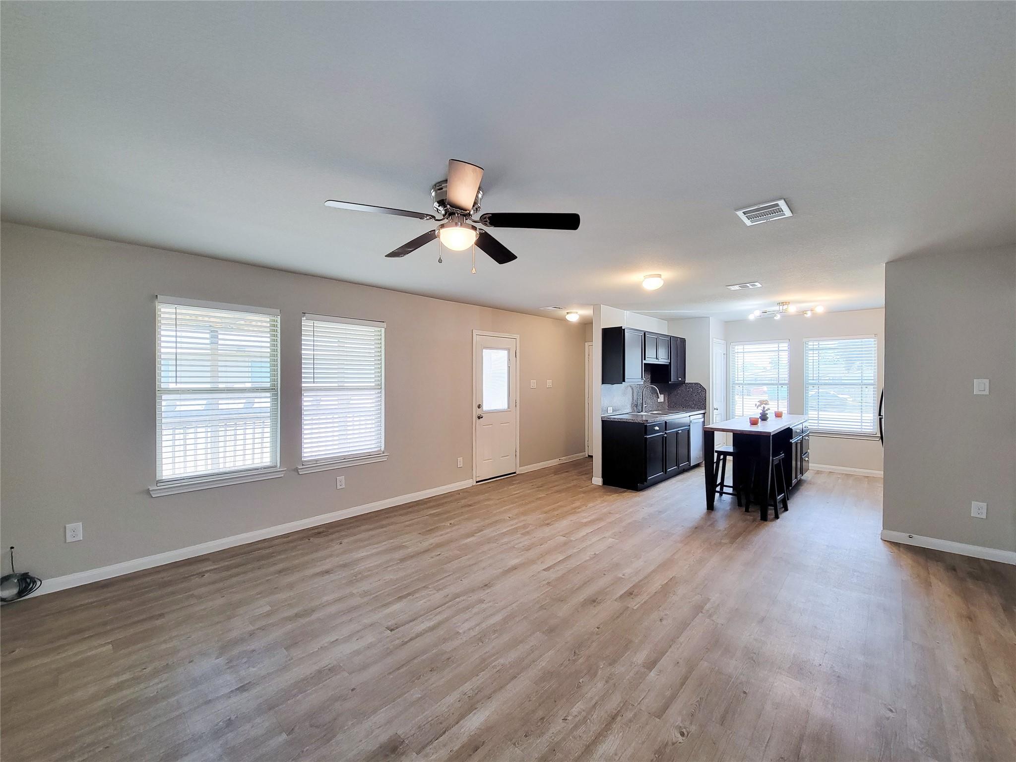 Open-plan living and dining area with wood-look floors, dark kitchen cabinets, and an island with bar stools.