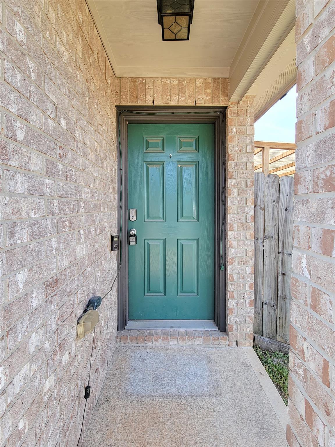 Brick home’s covered entry with a teal-green front door and keypad lock.
