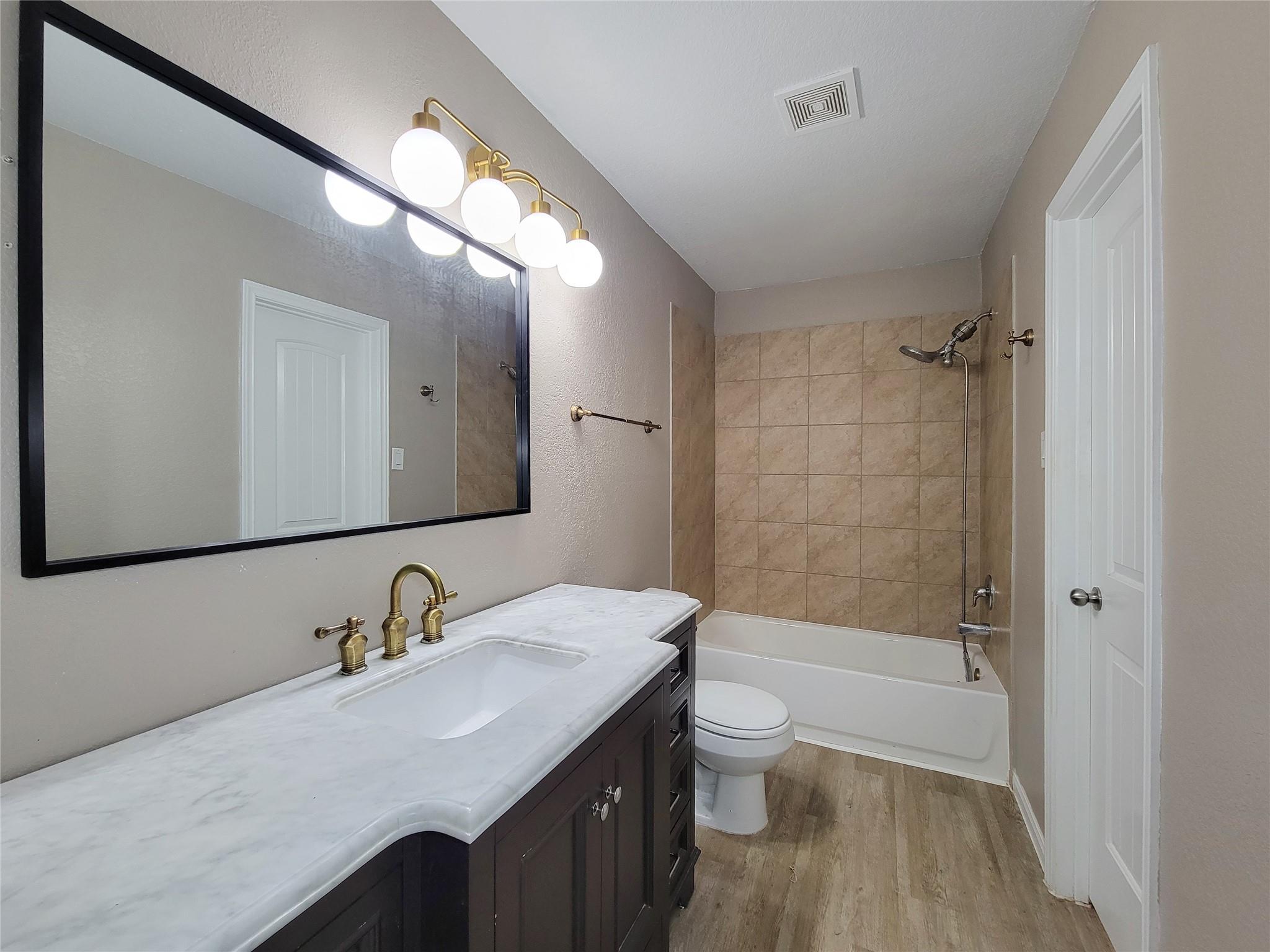 Bathroom with a dark vanity, large mirror, and tub with tan tiled shower surround.