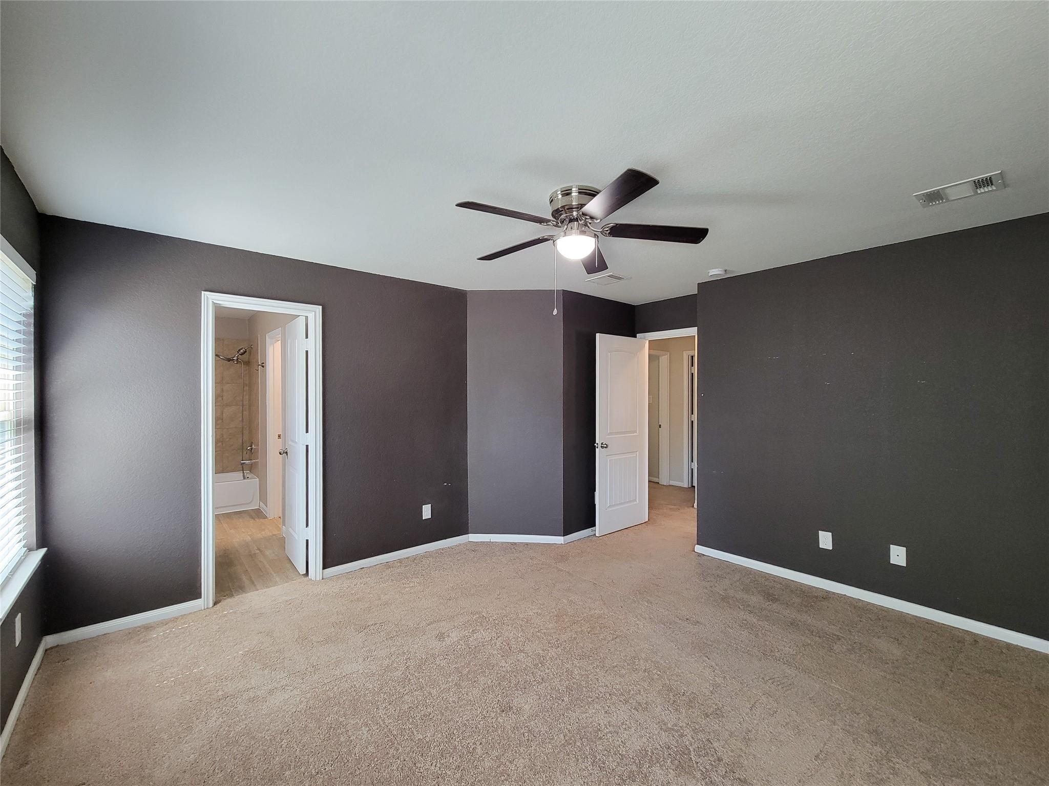 Empty bedroom with dark walls, beige carpet, ceiling fan, and open bathroom doorway.