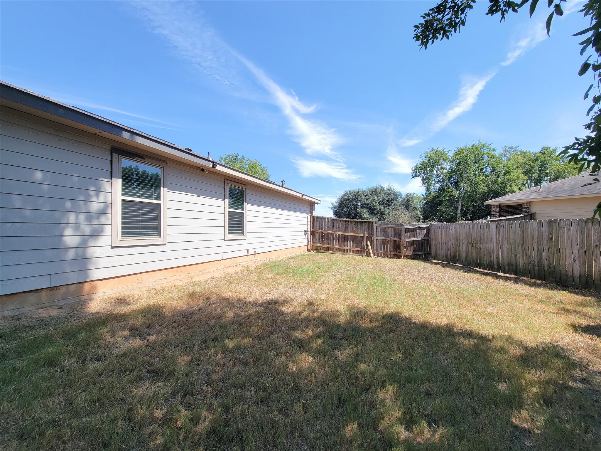 Fenced backyard beside a light-colored home, with two windows and a small fenced section at the far end.
