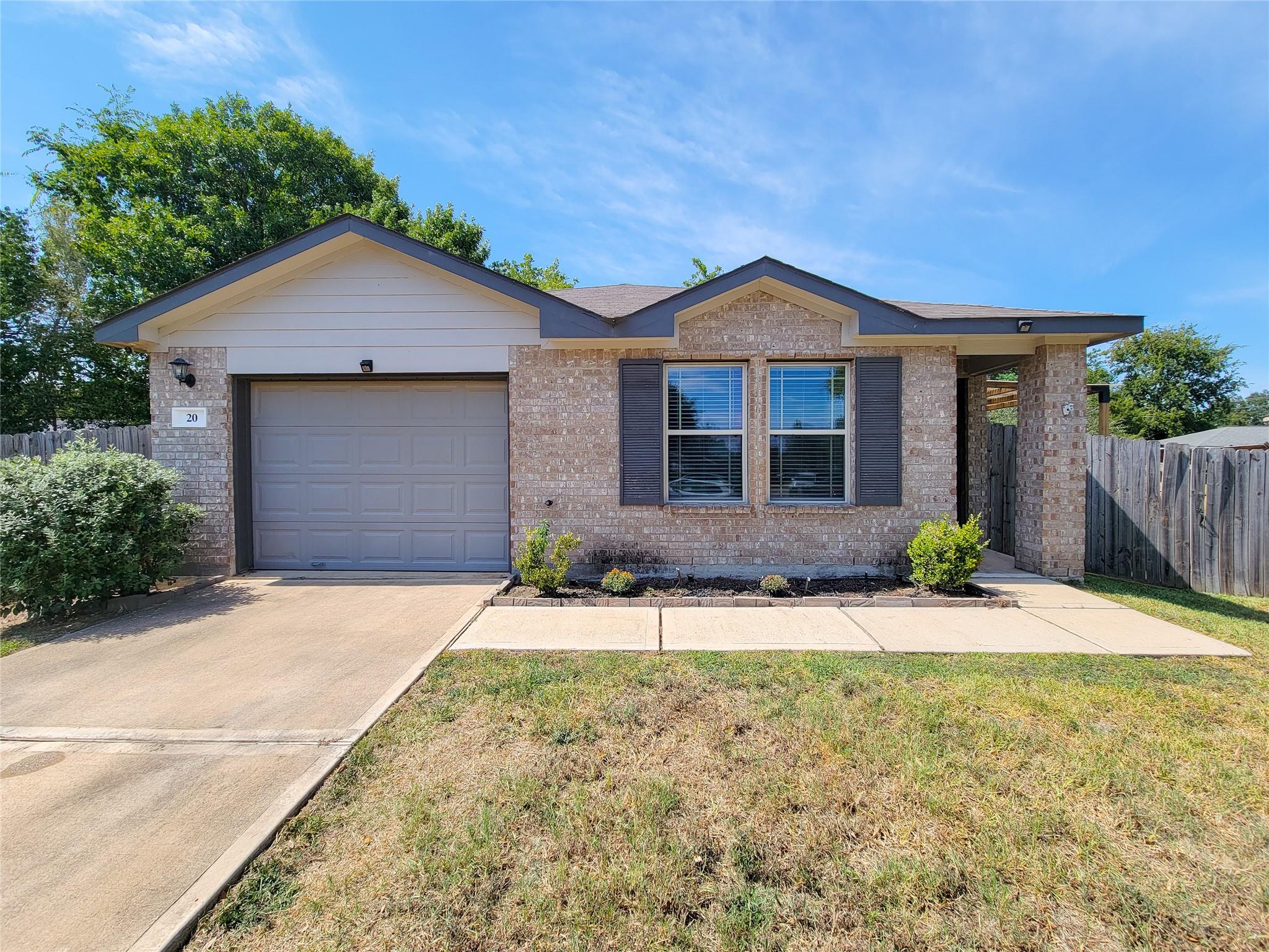 Single-story brick house with an attached garage, dark-shuttered windows, and a concrete driveway.
