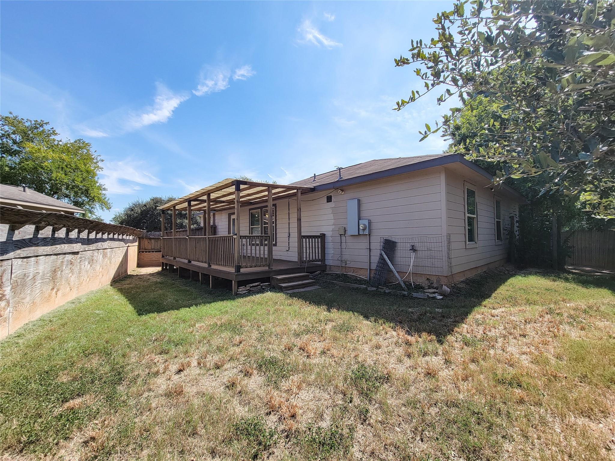 House rear with a raised wooden deck and pergola in a fenced backyard.