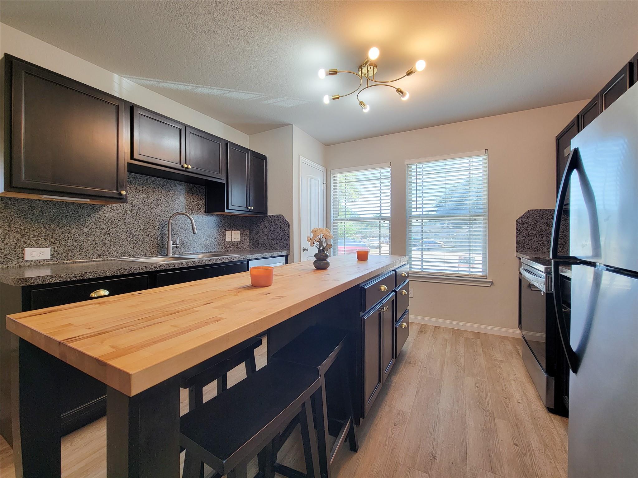 Kitchen with a large butcher-block island, dark cabinets, and stainless steel appliances.
