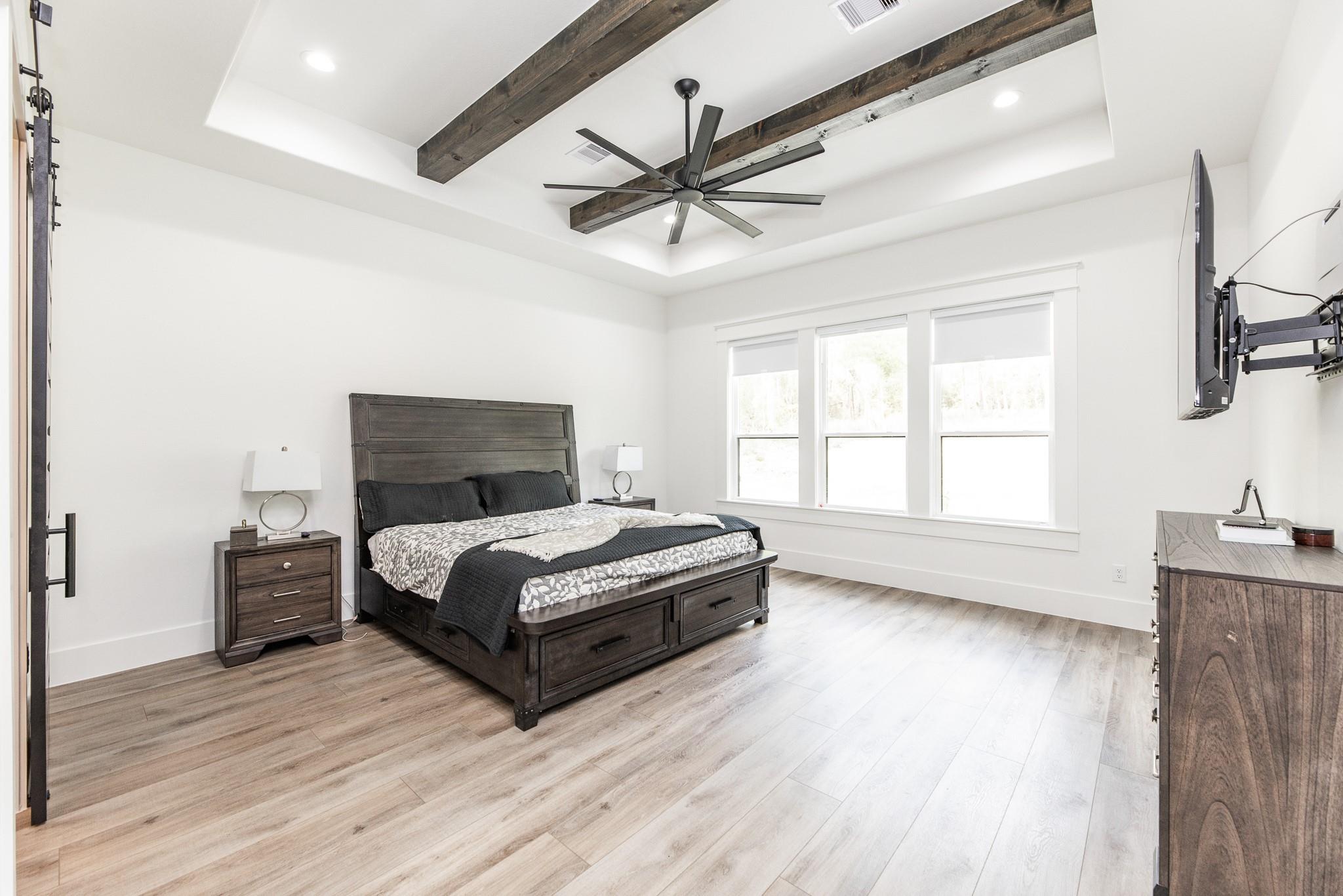 Bedroom with a dark wood storage bed, large windows, and exposed ceiling beams.