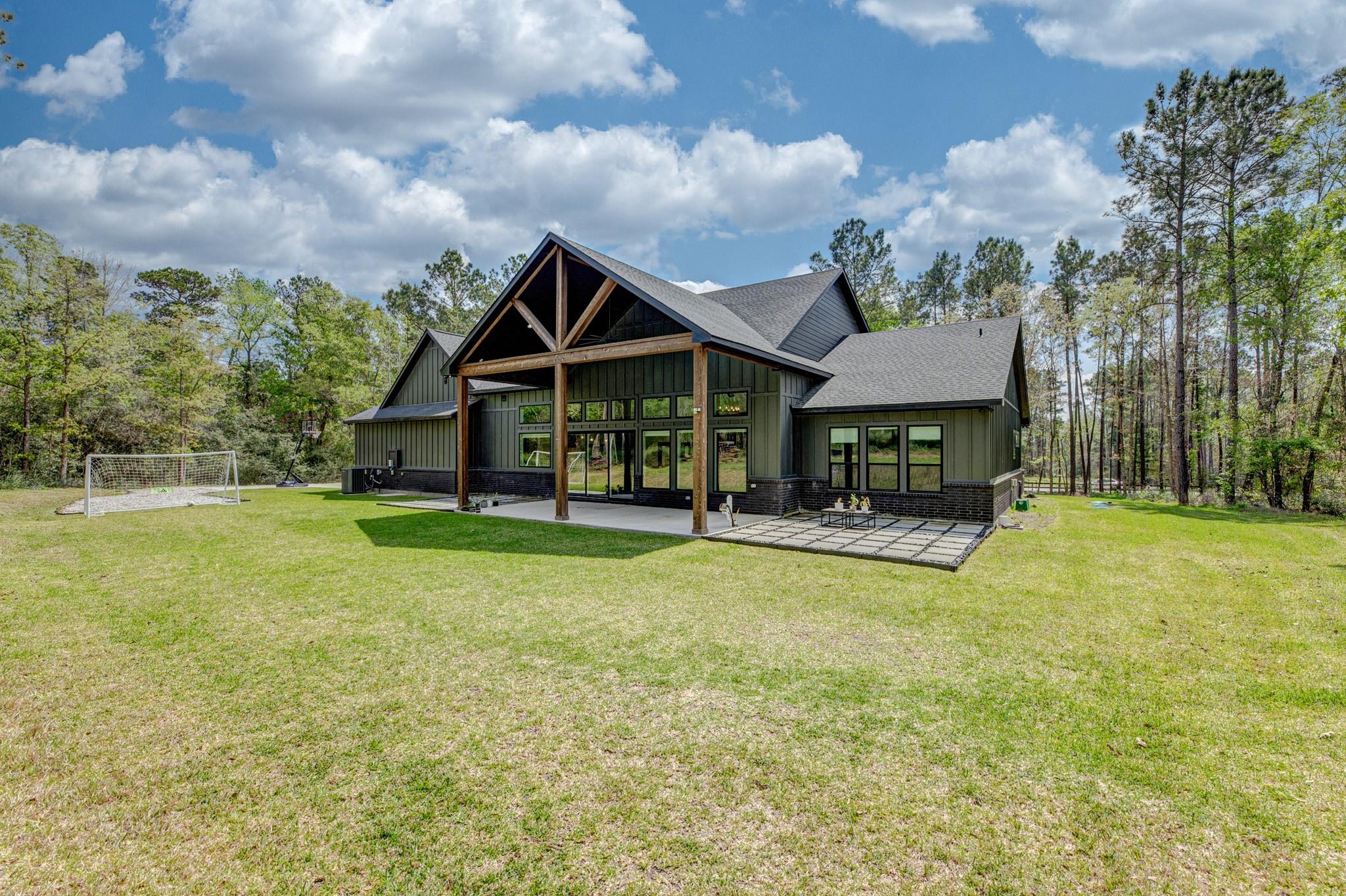 House with a timber-framed covered patio, broad lawn, and wooded backyard.
